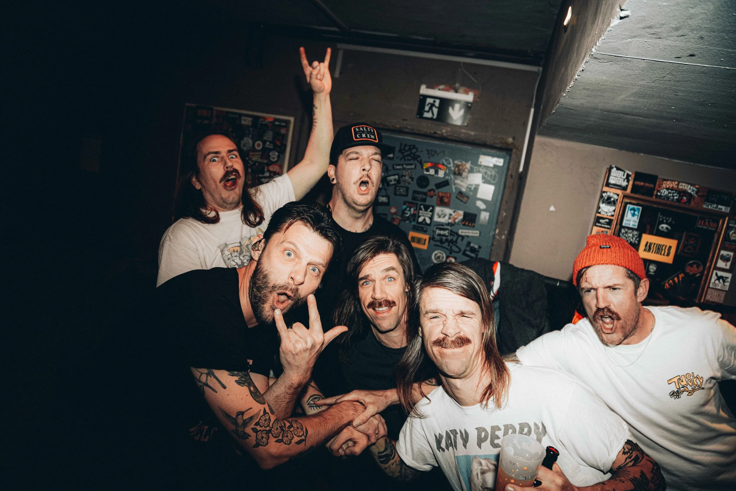 A group of six men posing together at a party, making various facial expressions up close.