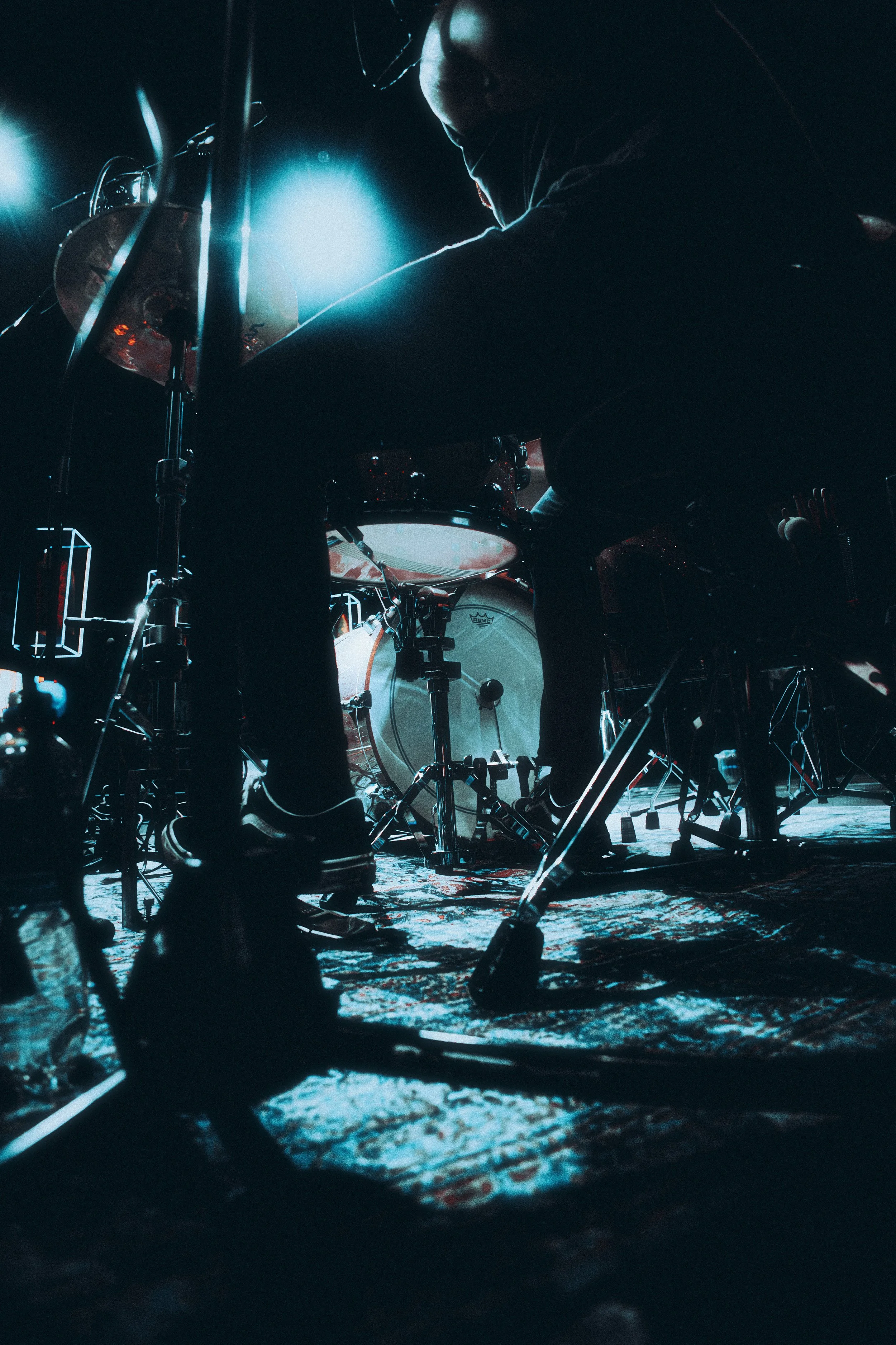 A person playing drums in a dark setting with blue lighting, focusing on the drum kit and their silhouette.