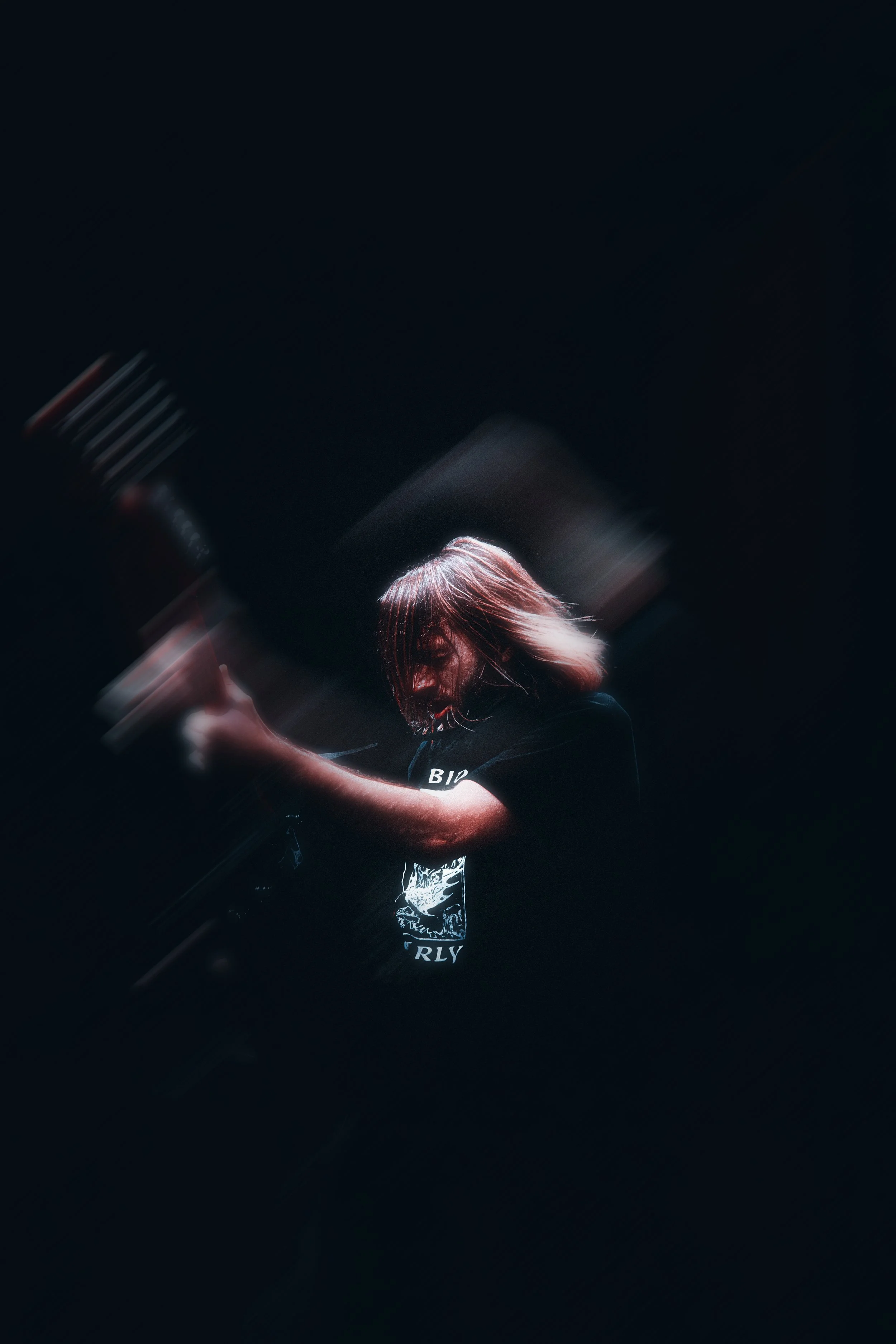 A woman with shoulder-length hair is playing an electric guitar in a dark environment, with dramatic lighting focused on her.