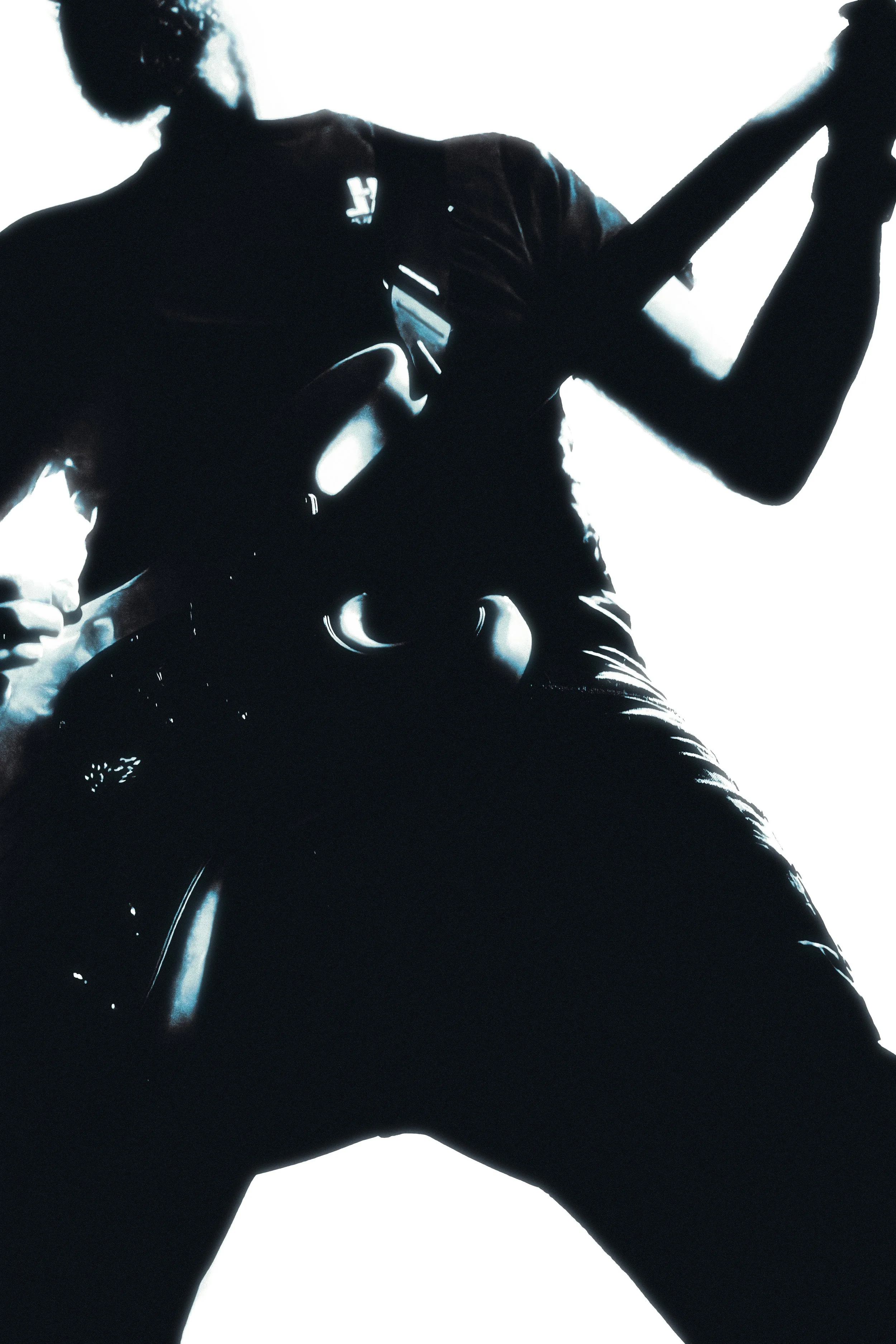 Silhouette of a person playing an electric guitar, posed dynamically against a bright light background, with the person’s arm raised and head slightly tilted.