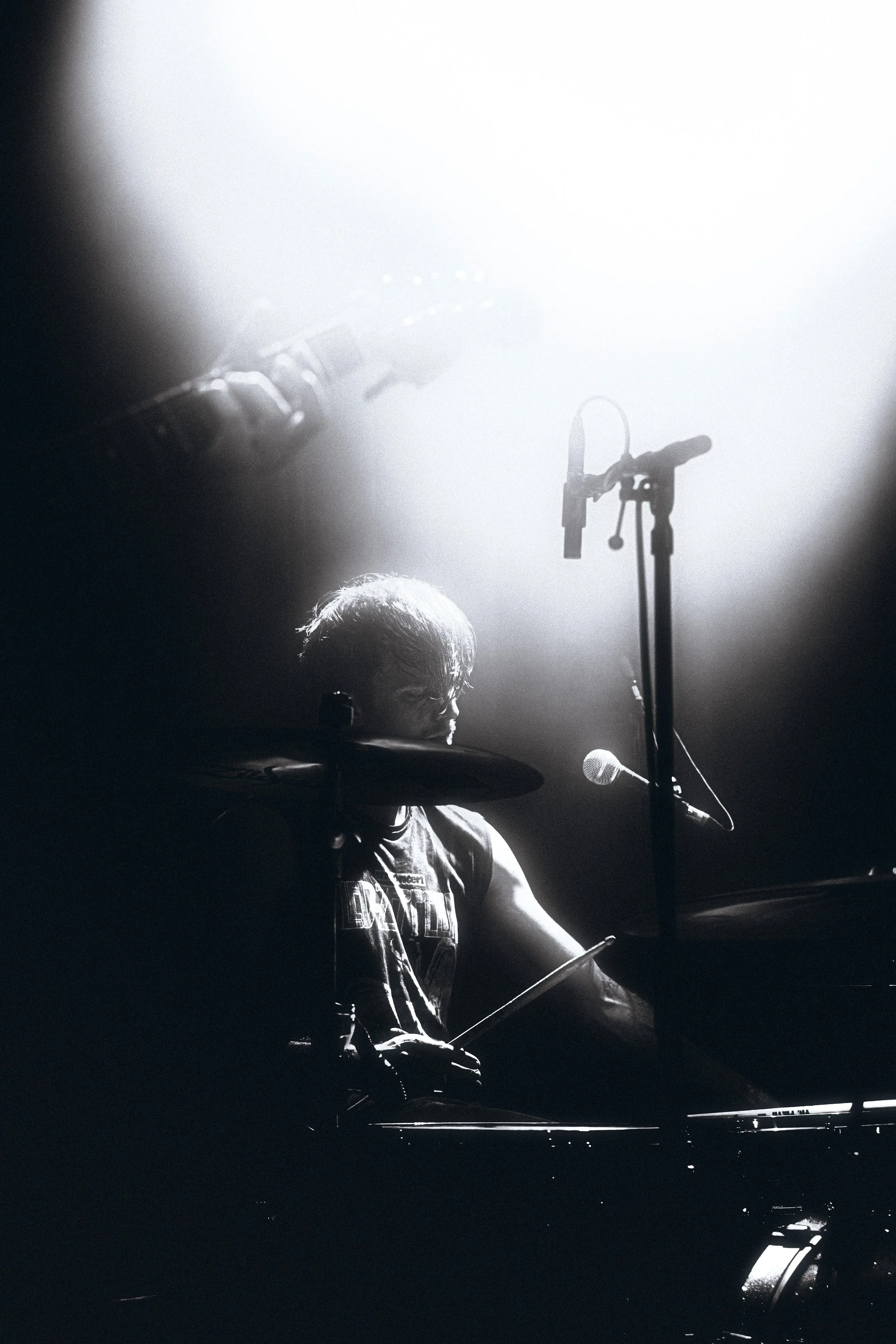 A musician playing drums on stage during a concert with bright stage lights creating a silhouette.