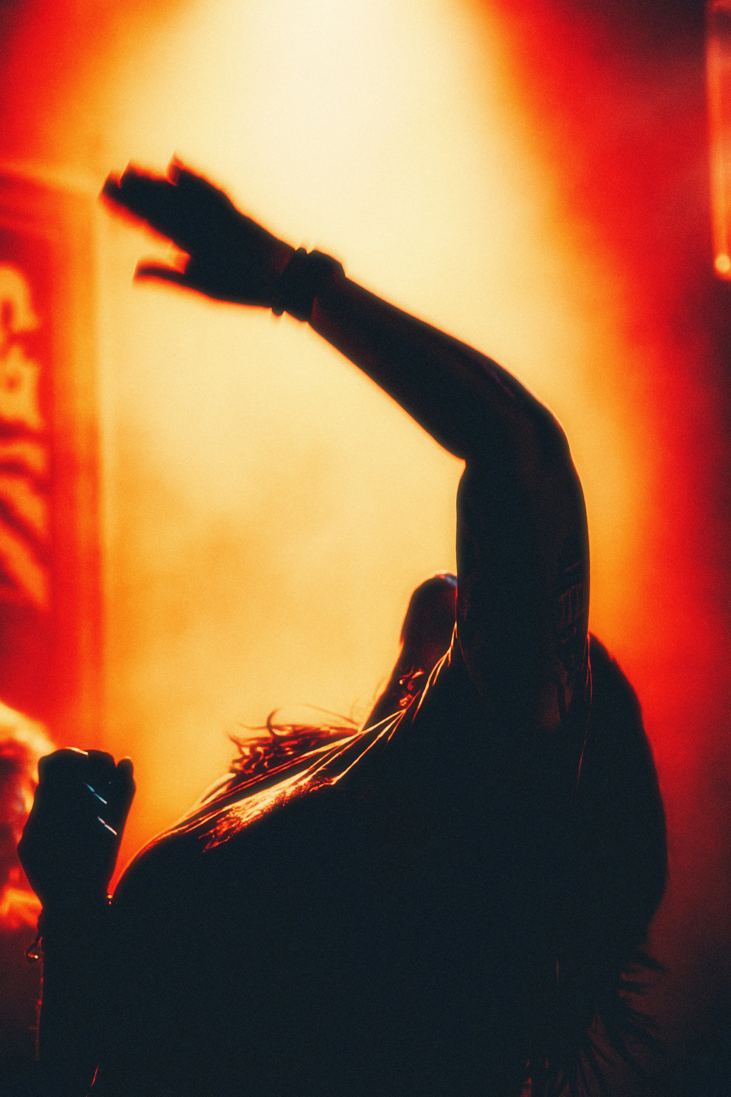 Silhouette of a person dancing against warm, orange backlighting.