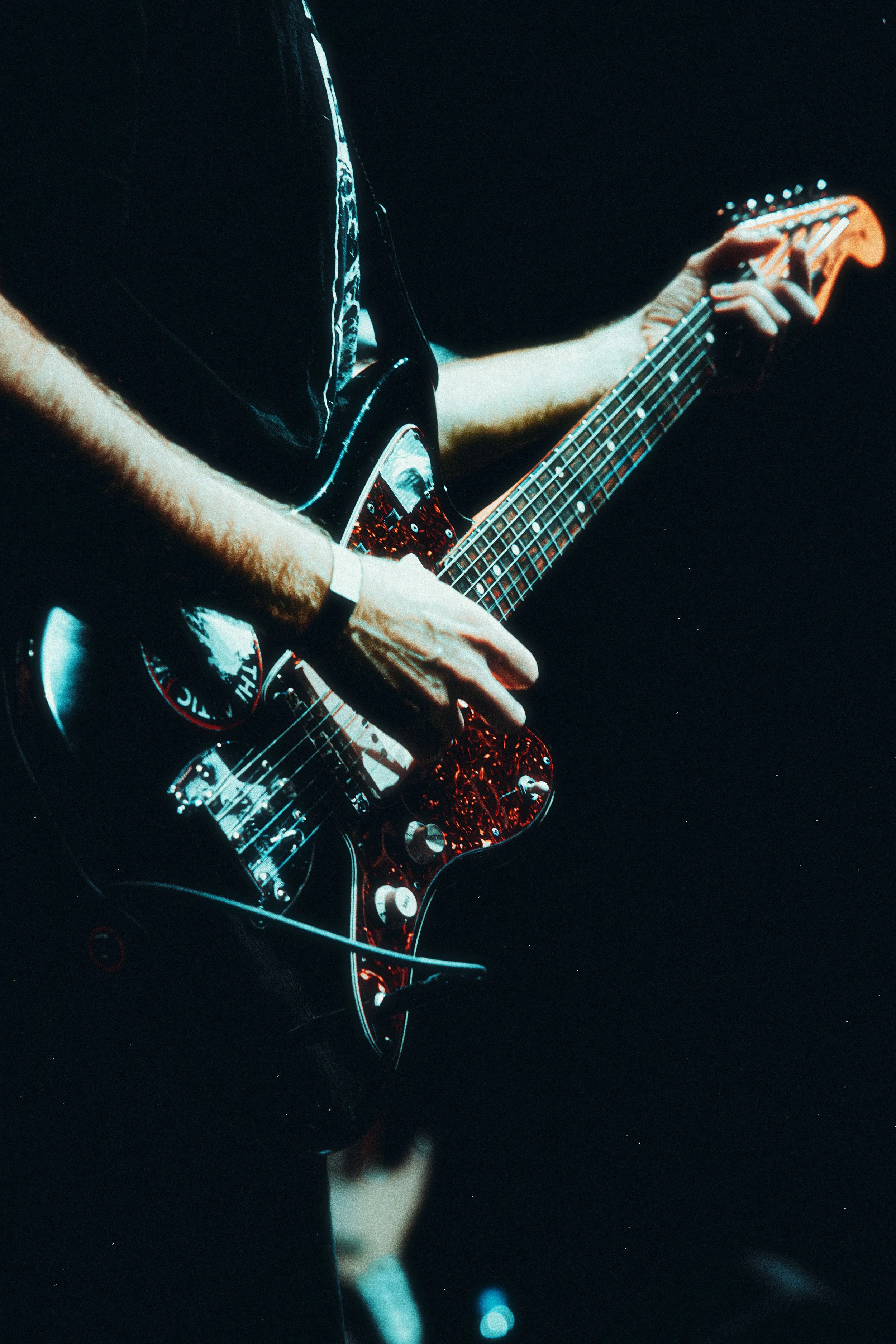 Close-up of a person playing an electric guitar in a dark setting.