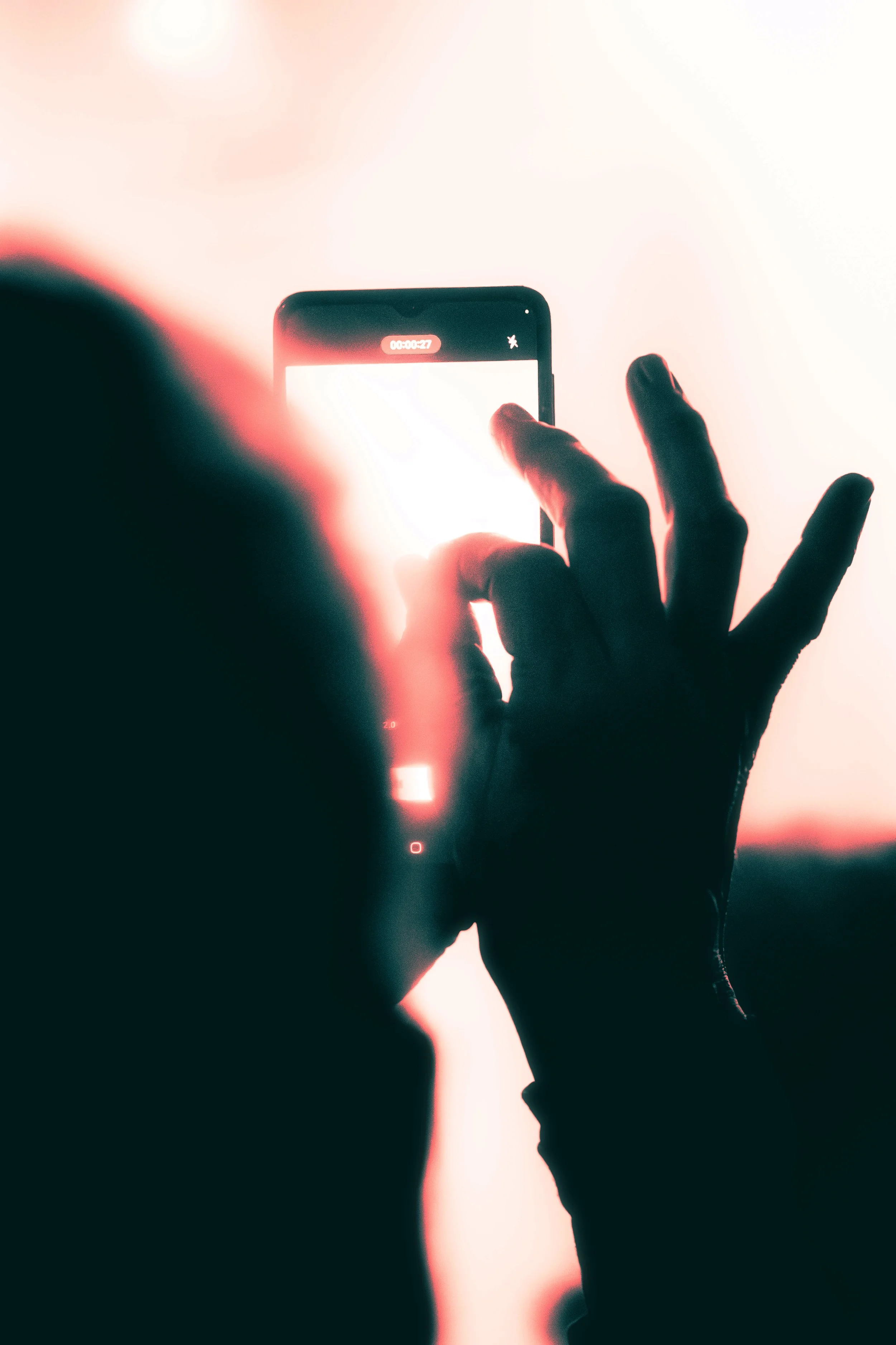 Person taking a photo with a smartphone, backlit scene with bright light.