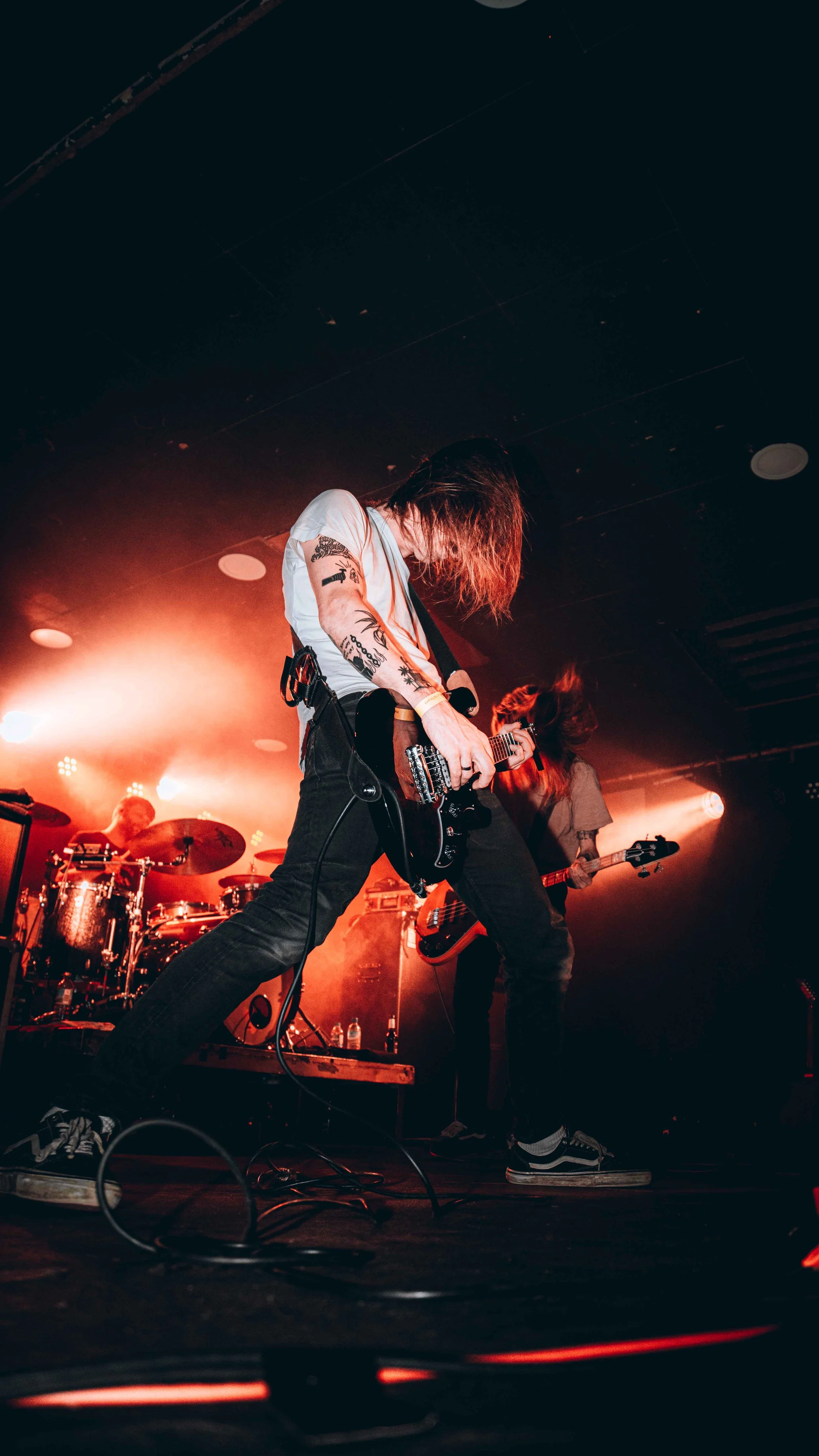 Musicians performing on stage with guitars and drums, with orange stage lighting creating a lively atmosphere.