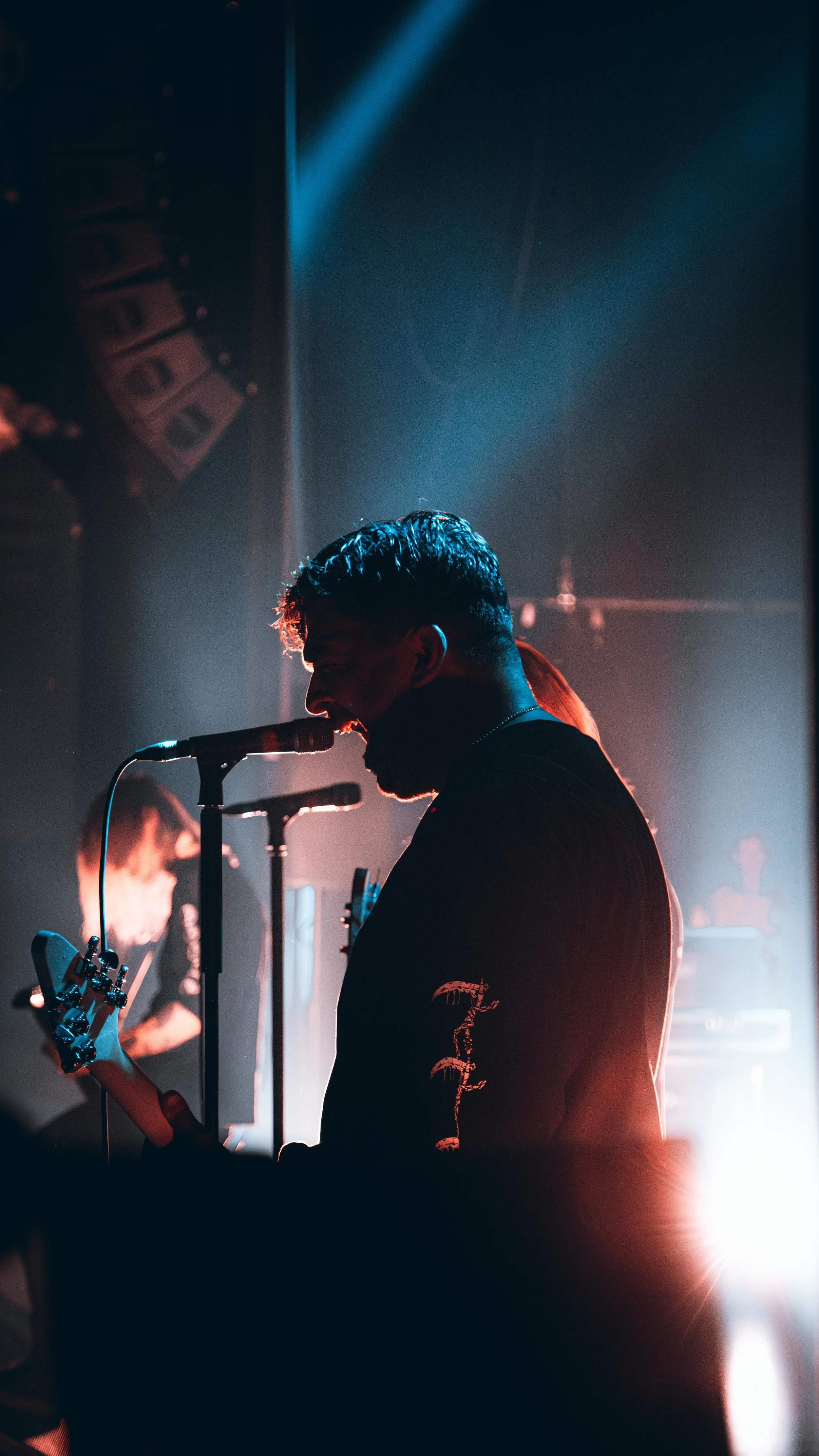 Musician singing into a microphone while playing a guitar on stage with dramatic lighting.