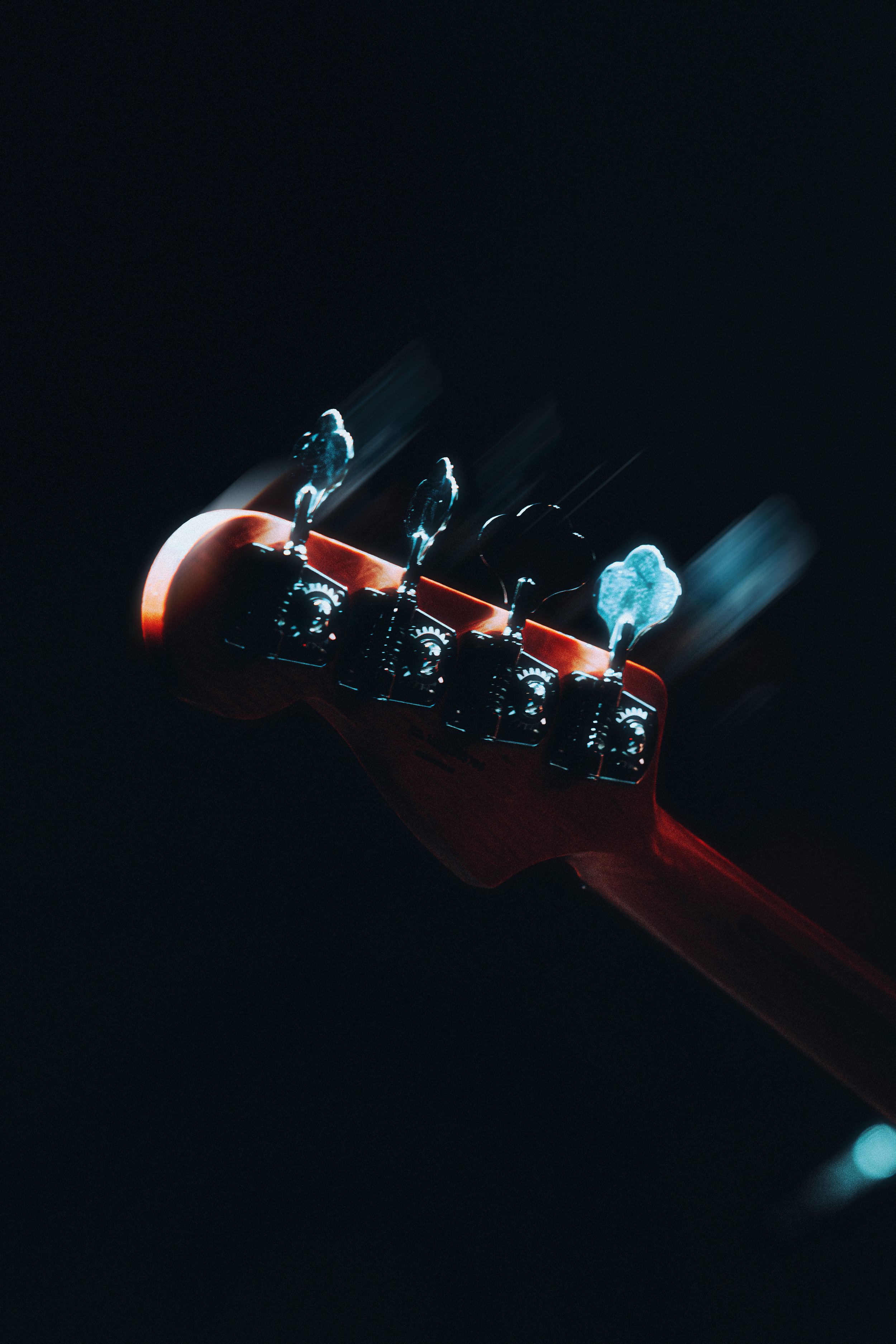Close-up of a red electric guitar headstock with tuning pegs, reflected in a dark background.