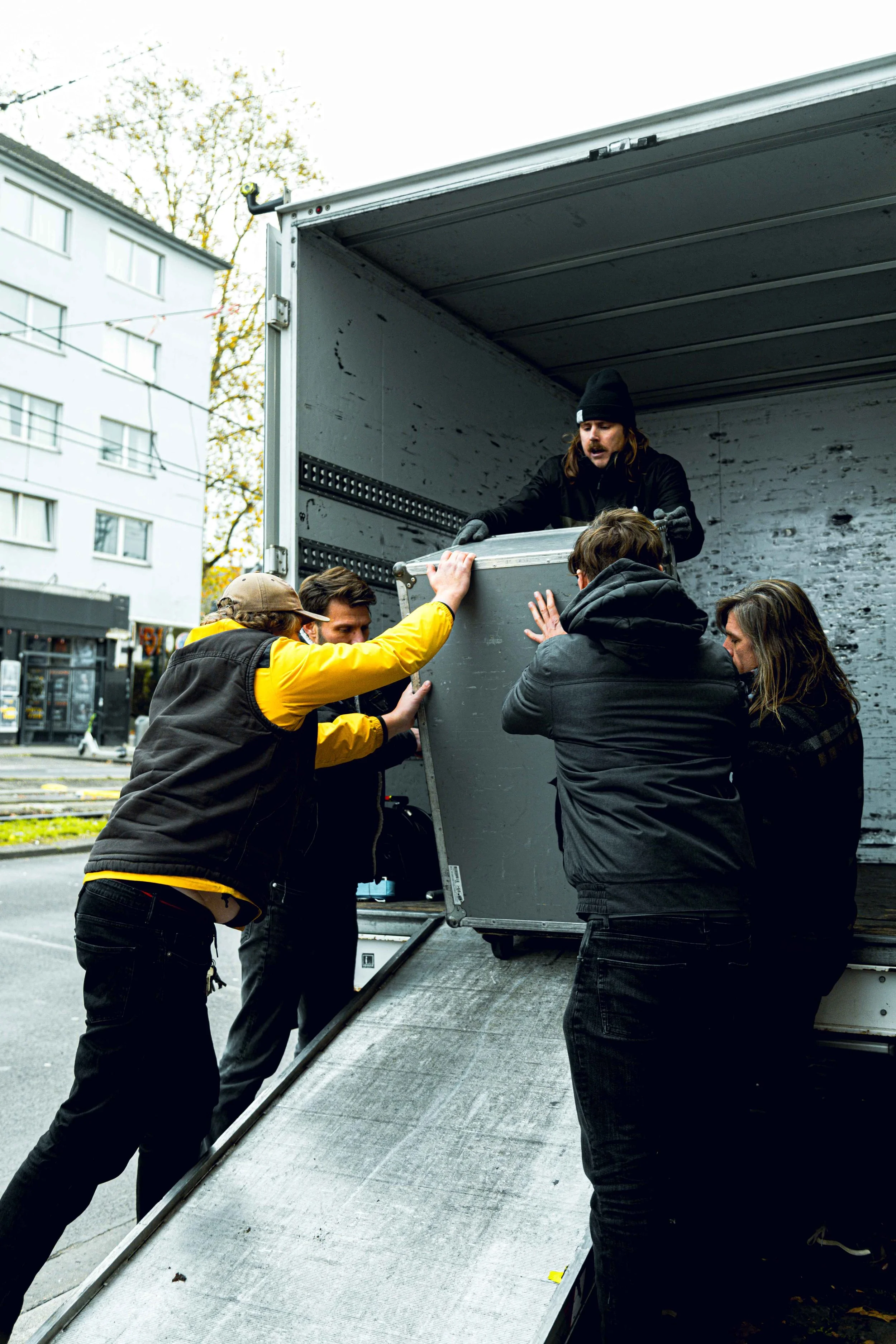 People helping to unload a large piece of furniture from a moving truck on a city street.