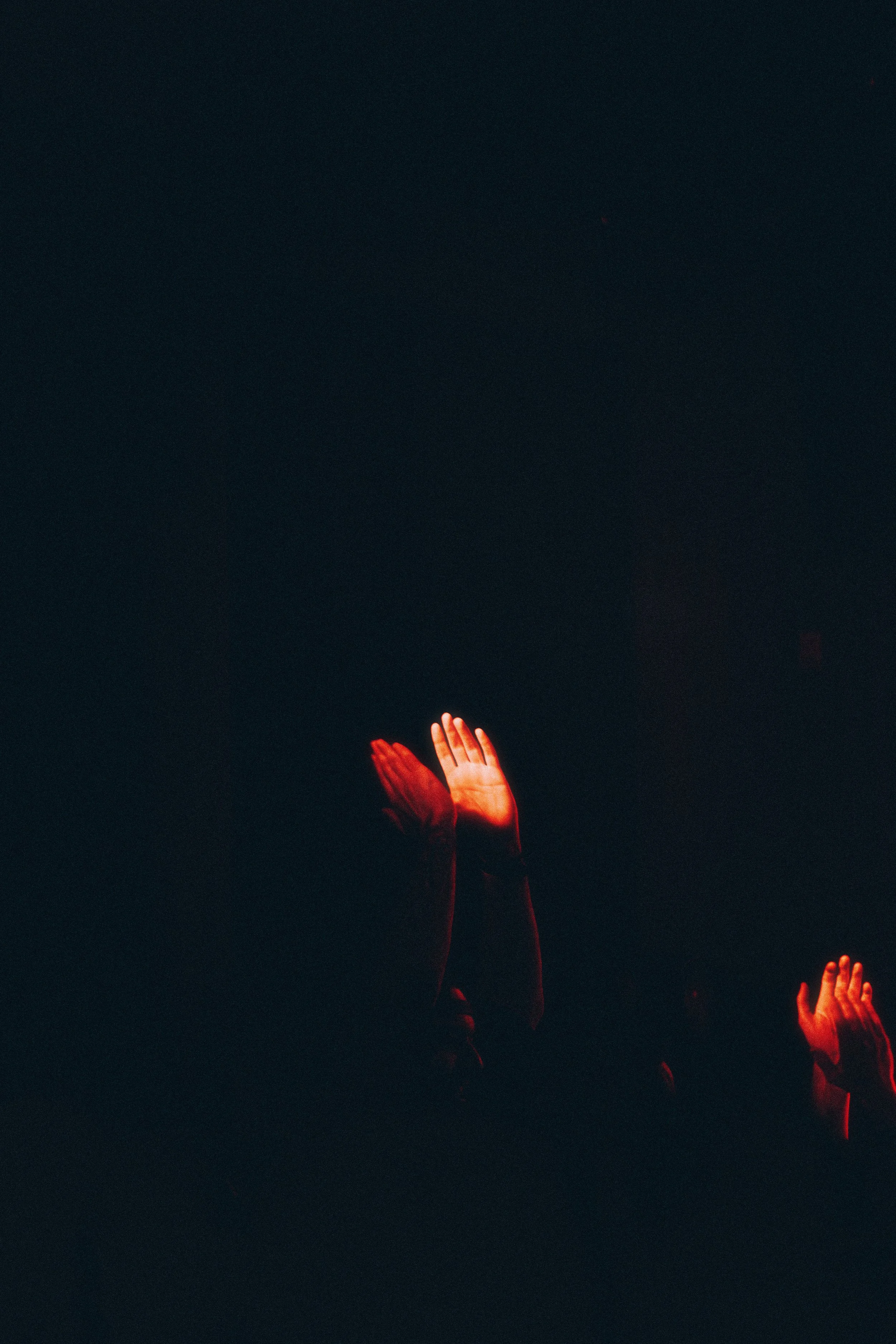 Hands with palms together, illuminated by red light, in a dark environment.
