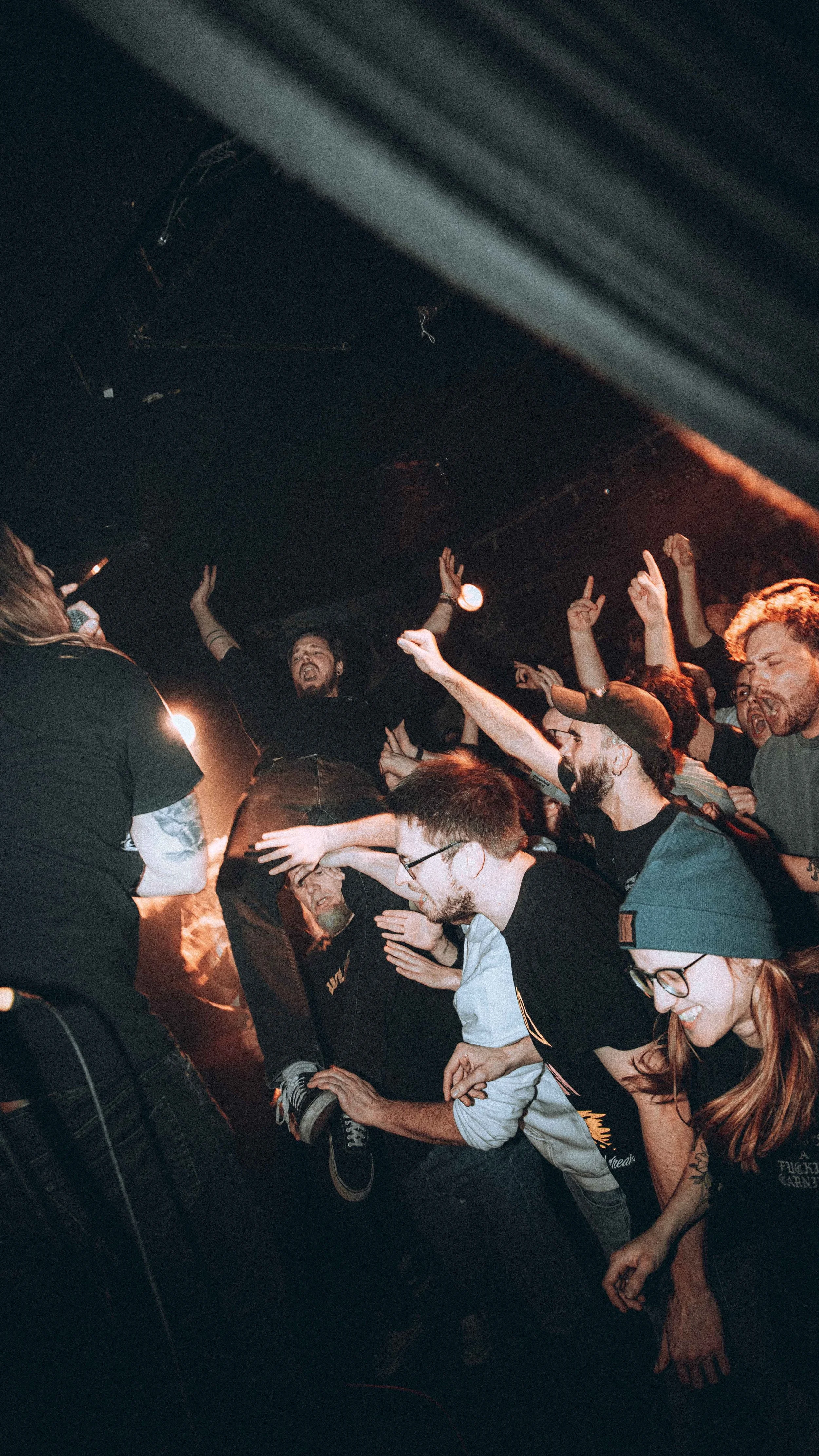 Crowd of people dancing and enjoying a concert in a dark indoor venue.