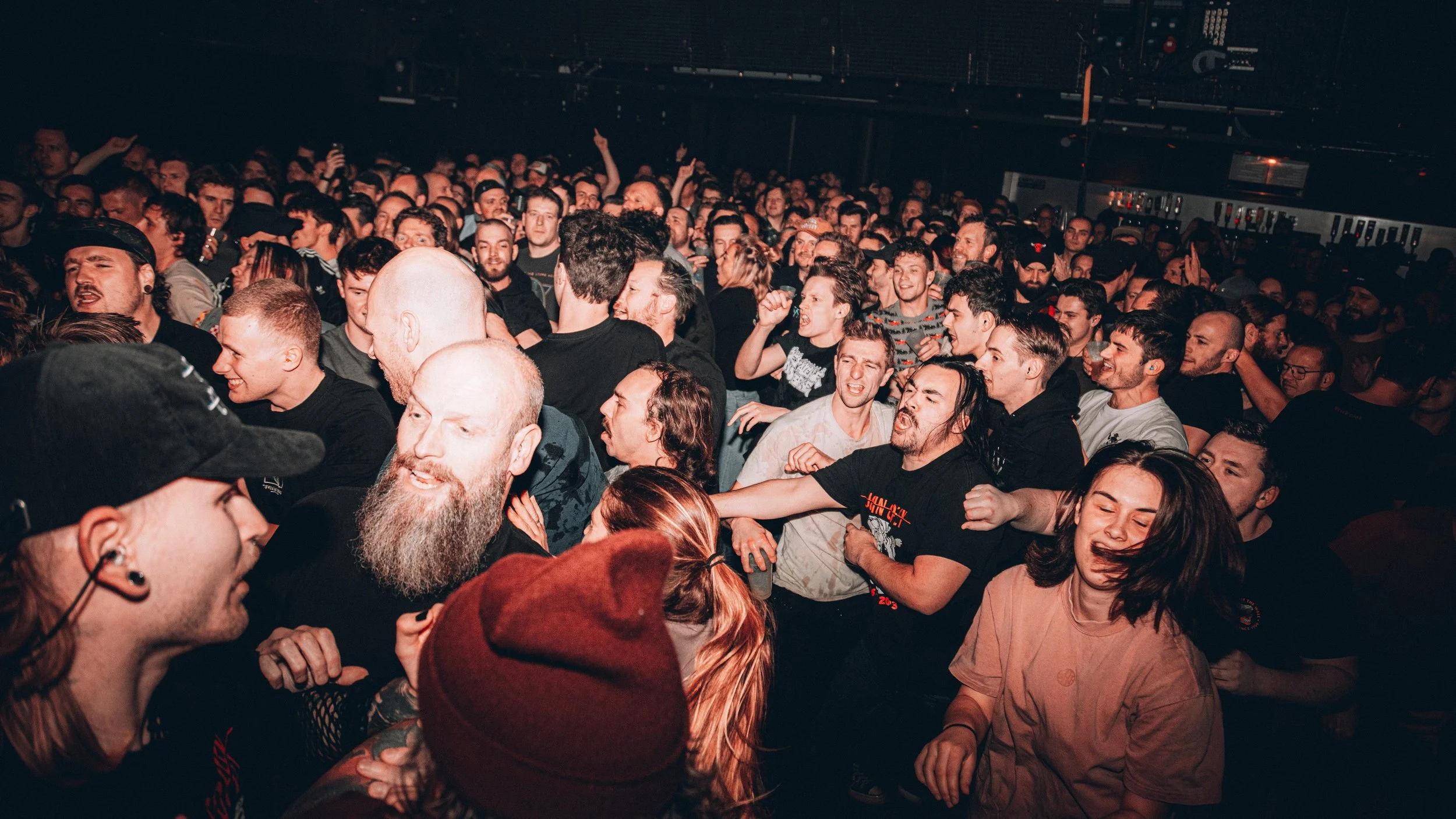 Crowded concert crowd enjoying music, with some people dancing and others singing, in a dark indoor venue.