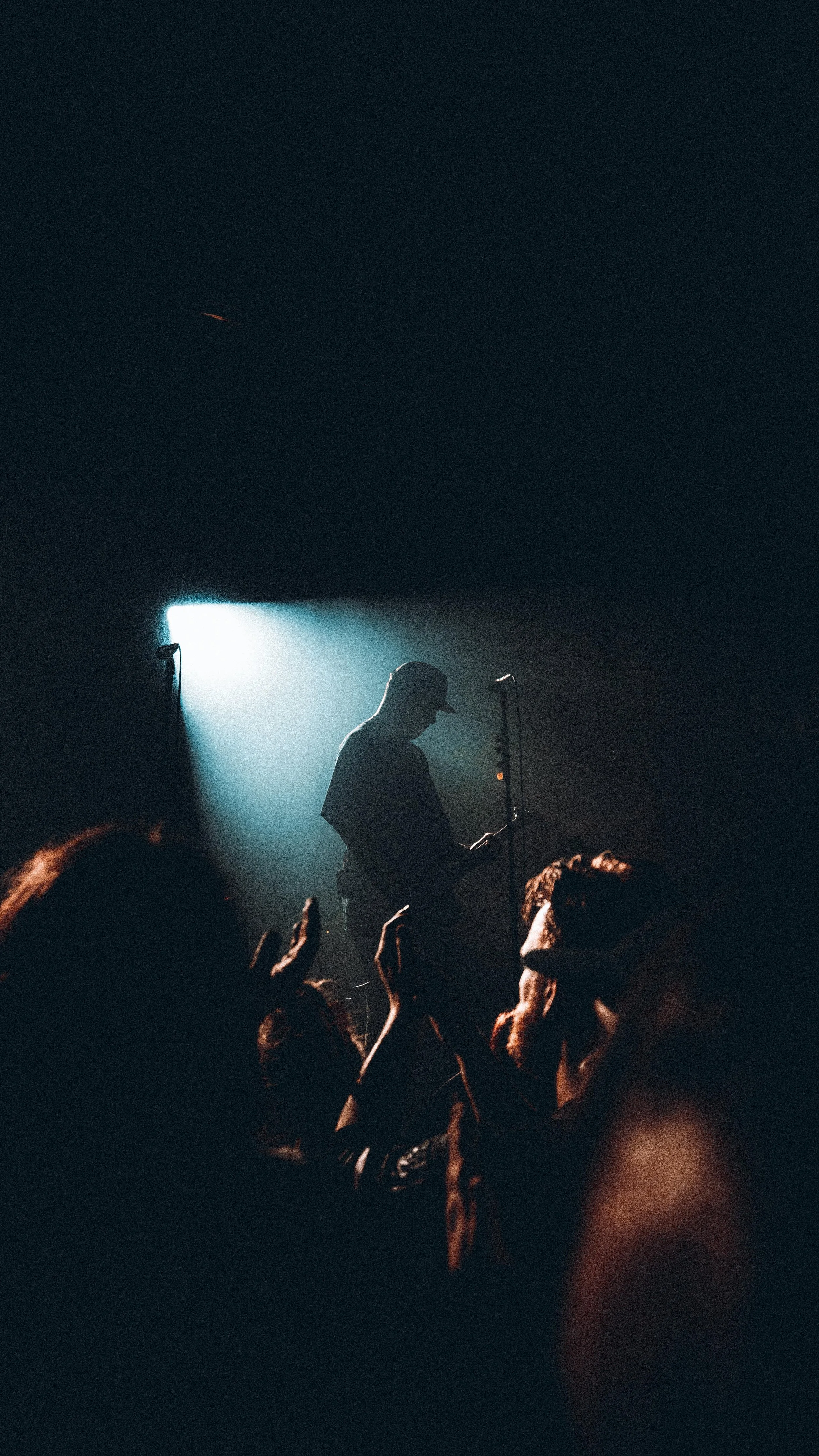 Silhouette of a musician playing guitar on stage with a spotlight behind him, surrounded by an audience.