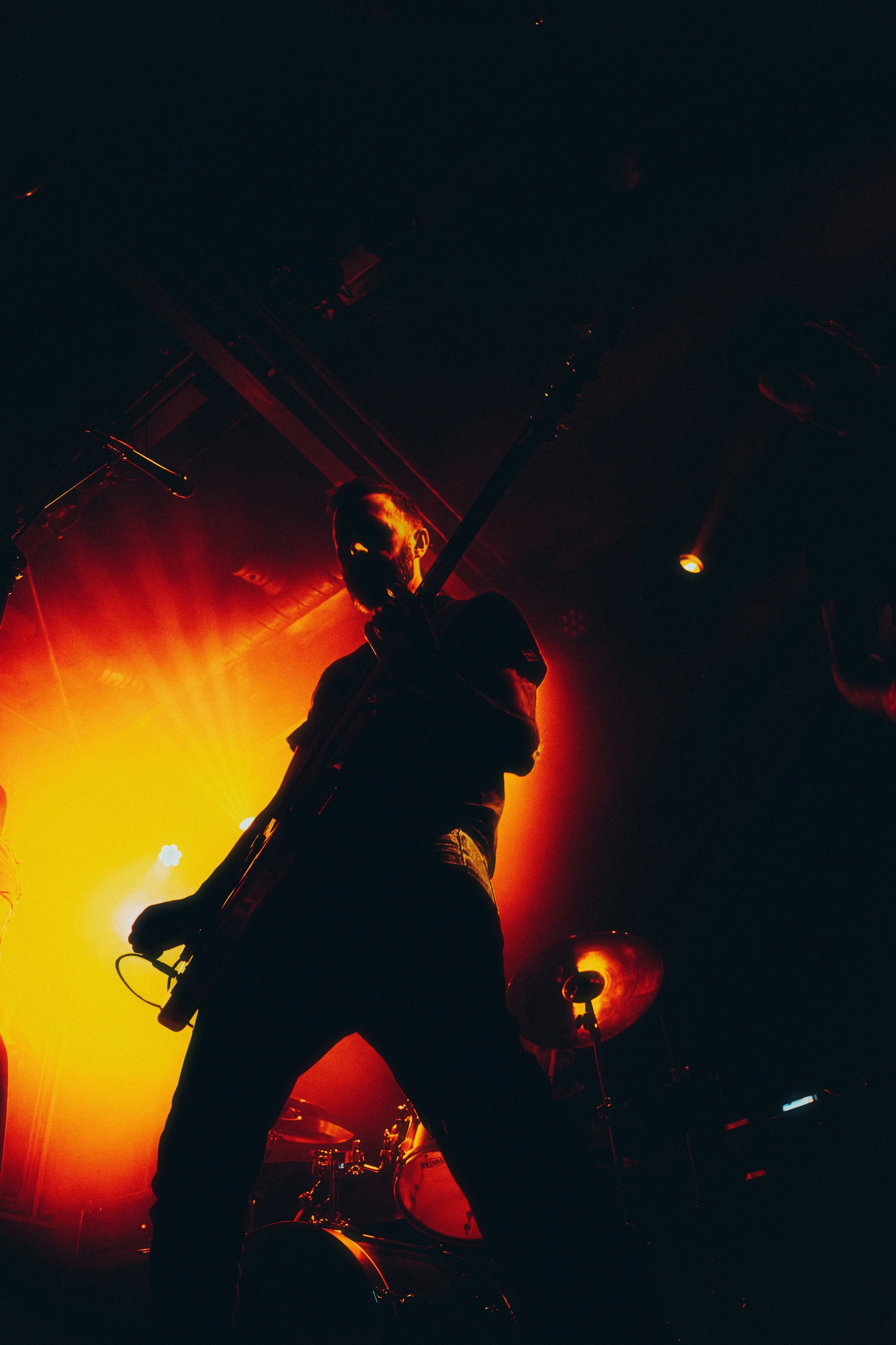 Silhouette of a musician playing guitar on stage with orange and yellow lighting.