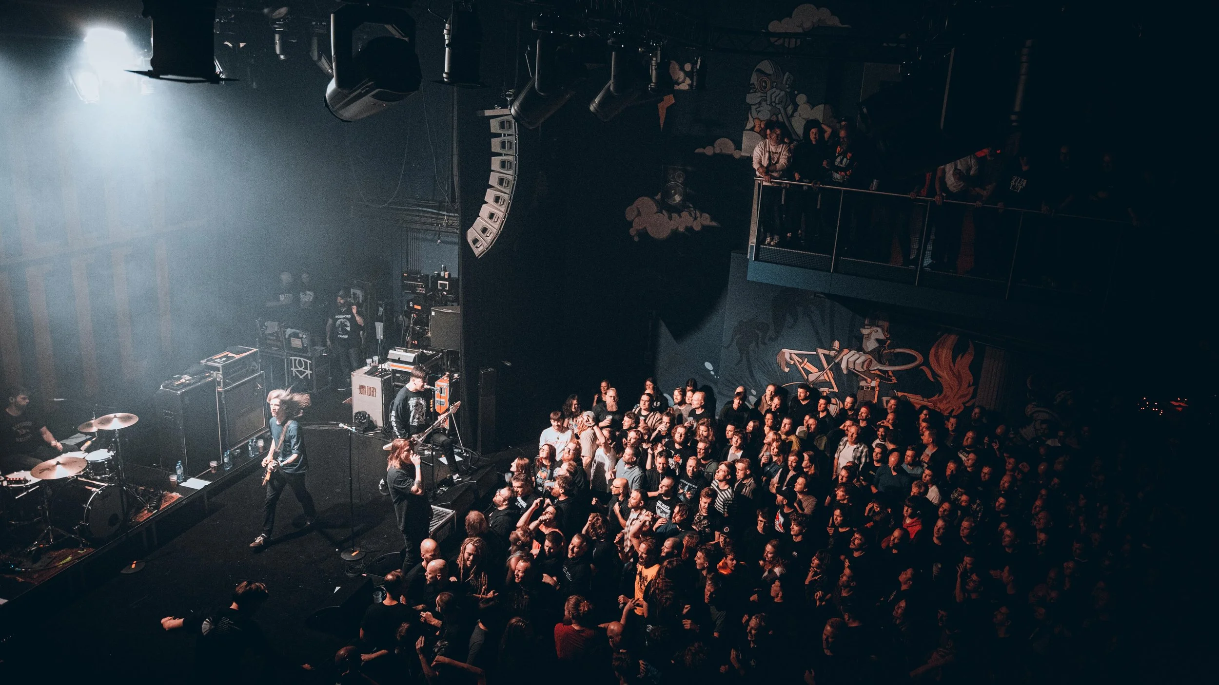 A crowd watching a band perform on stage at a concert venue with dark lighting.