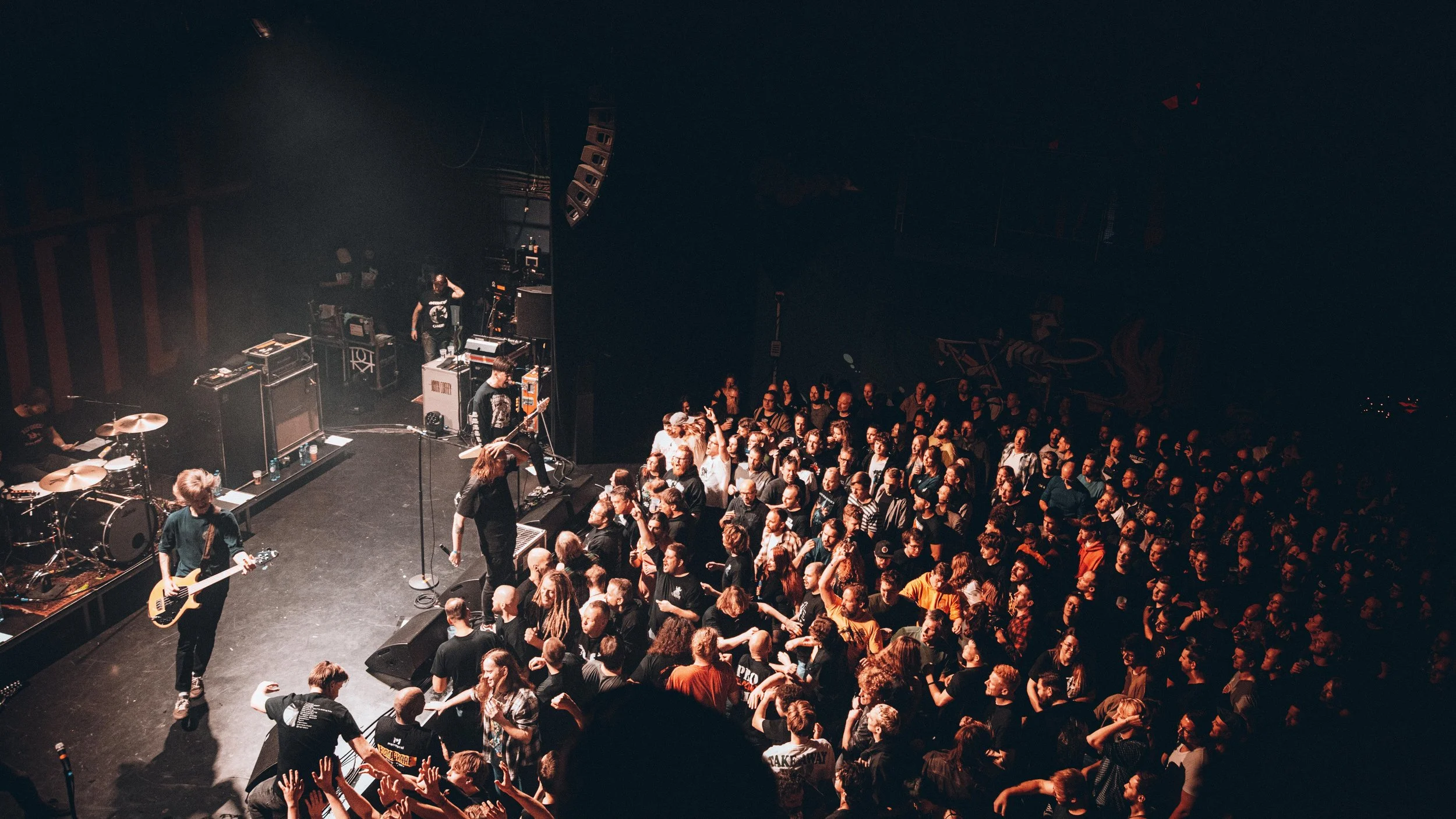 Music concert with a band performing on stage and a crowd of fans watching in a dimly lit venue.