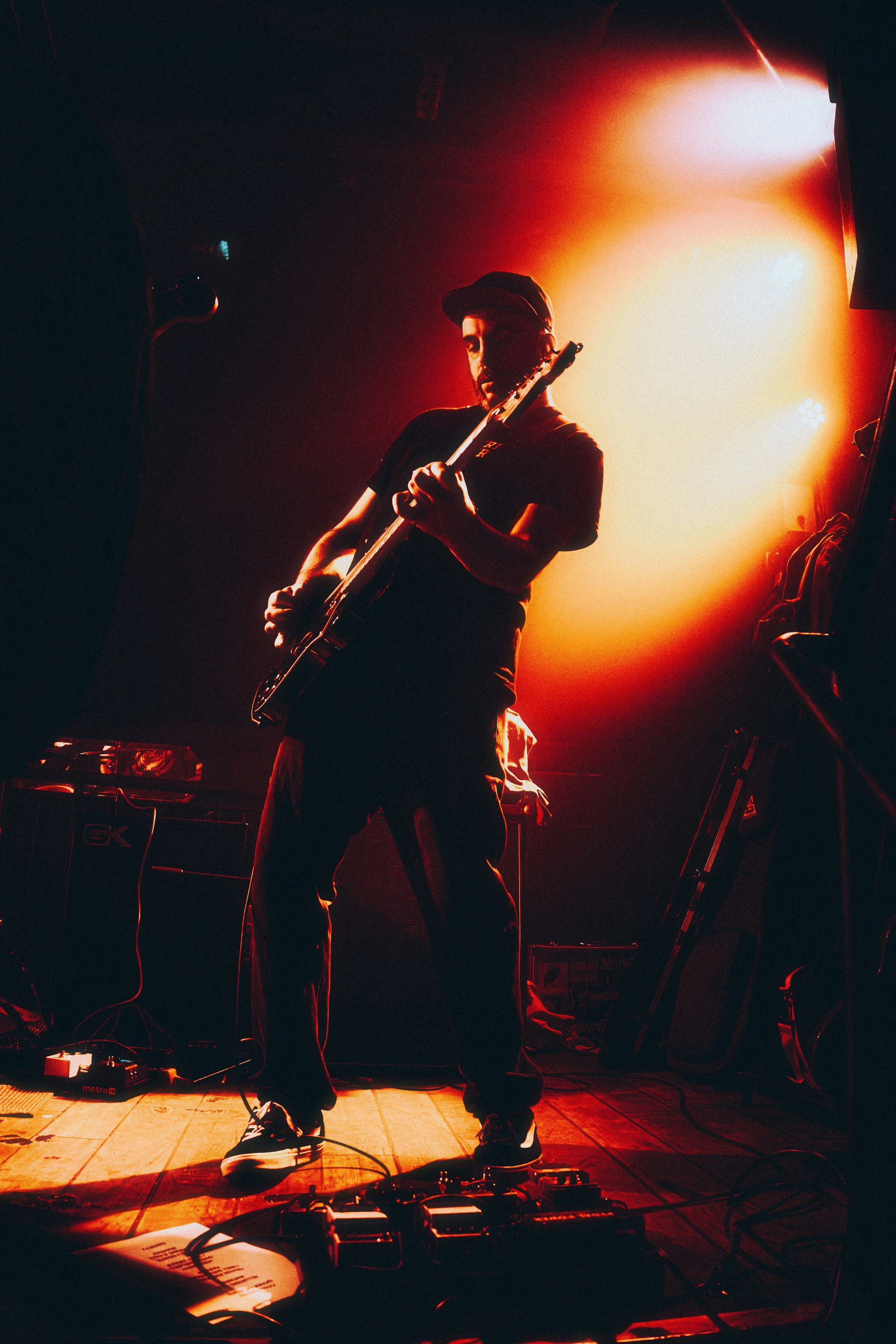 Musician playing guitar on stage with orange and red lighting effects.