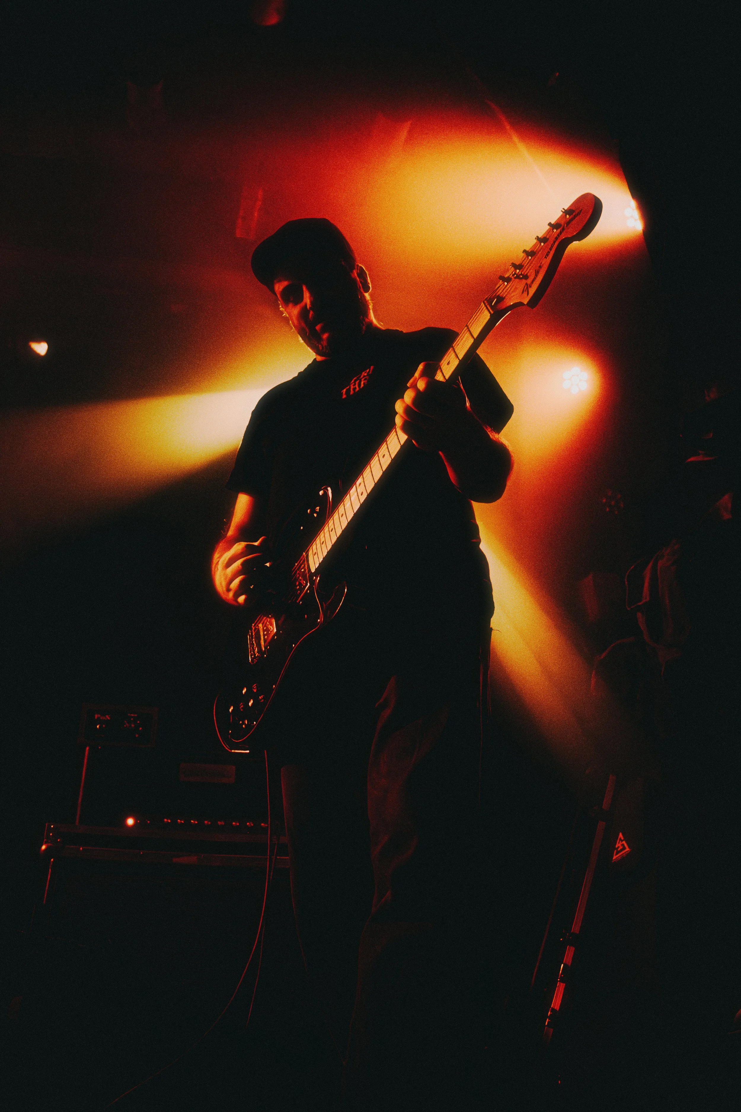 A person playing an electric guitar on stage with dramatic lighting that creates a silhouette effect.