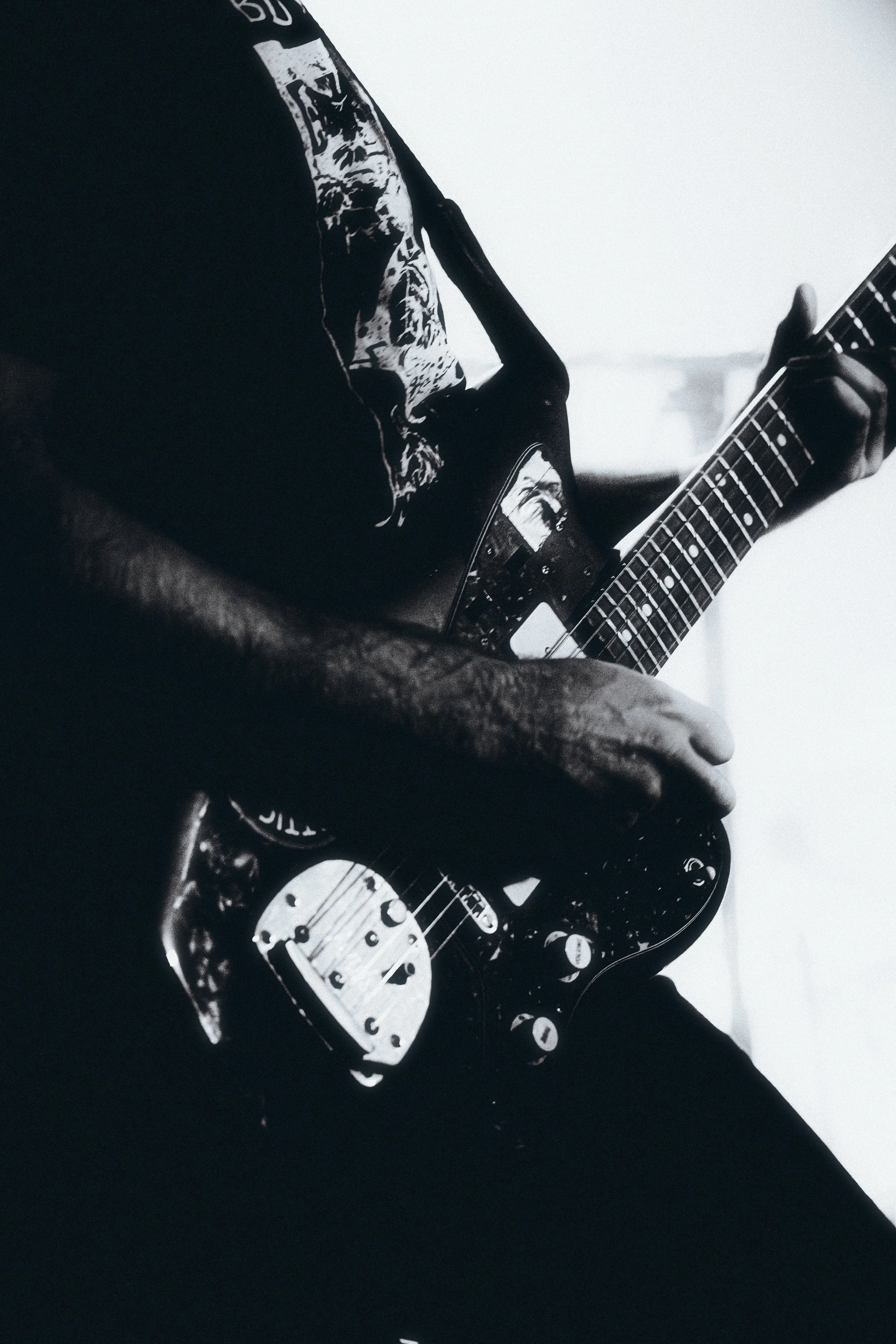 A person playing an electric guitar, captured in black and white, with focus on their hands and the guitar.