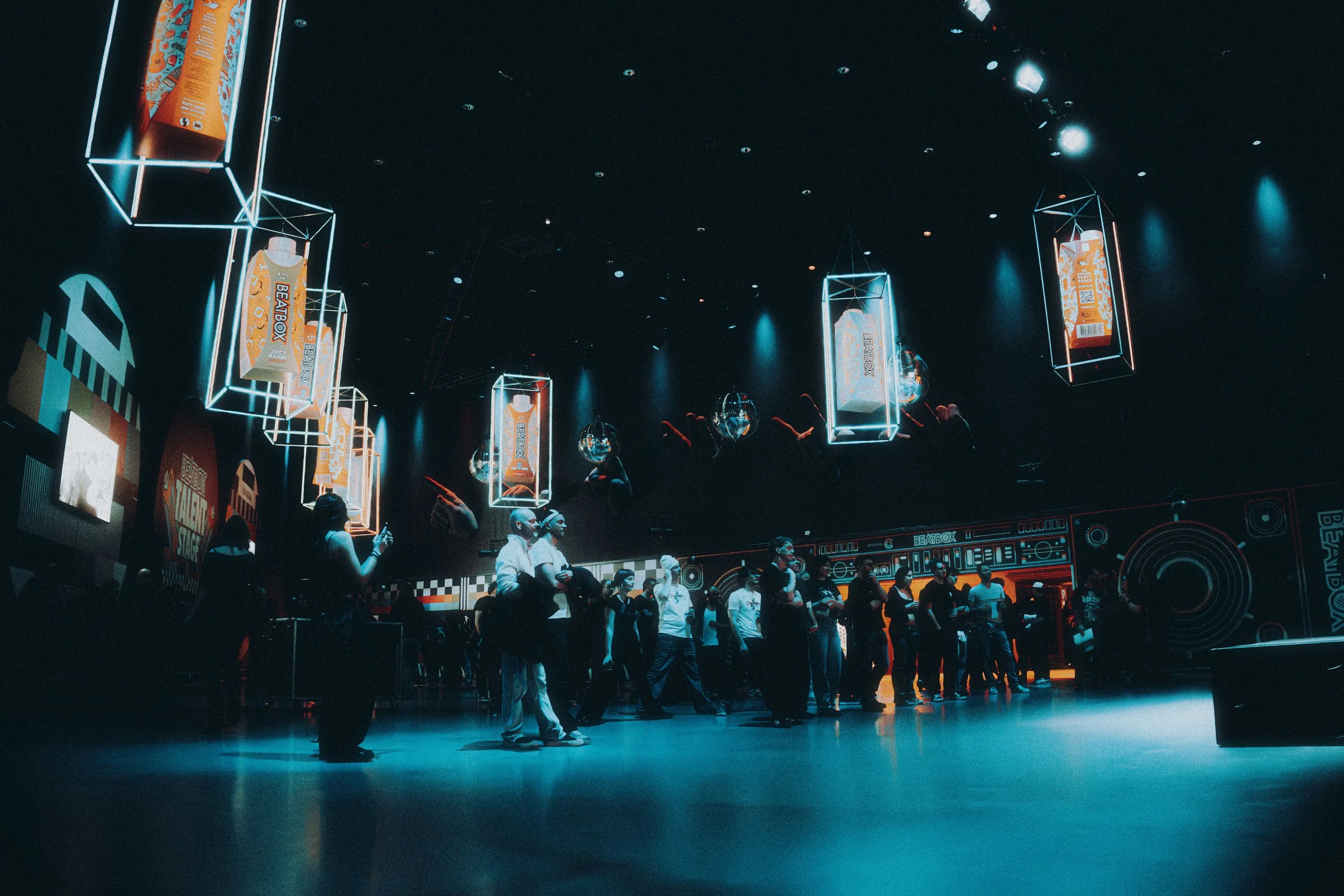 People lined up indoors with BC Kids snacks hanging from illuminated display frames on the ceiling.