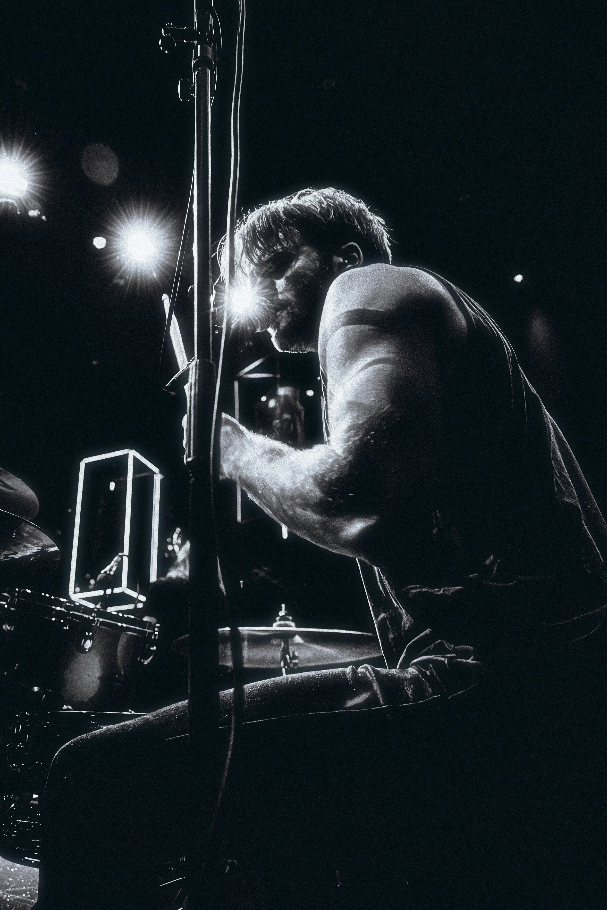 A black and white photo of a musician playing the drums on stage, illuminated by stage lights.