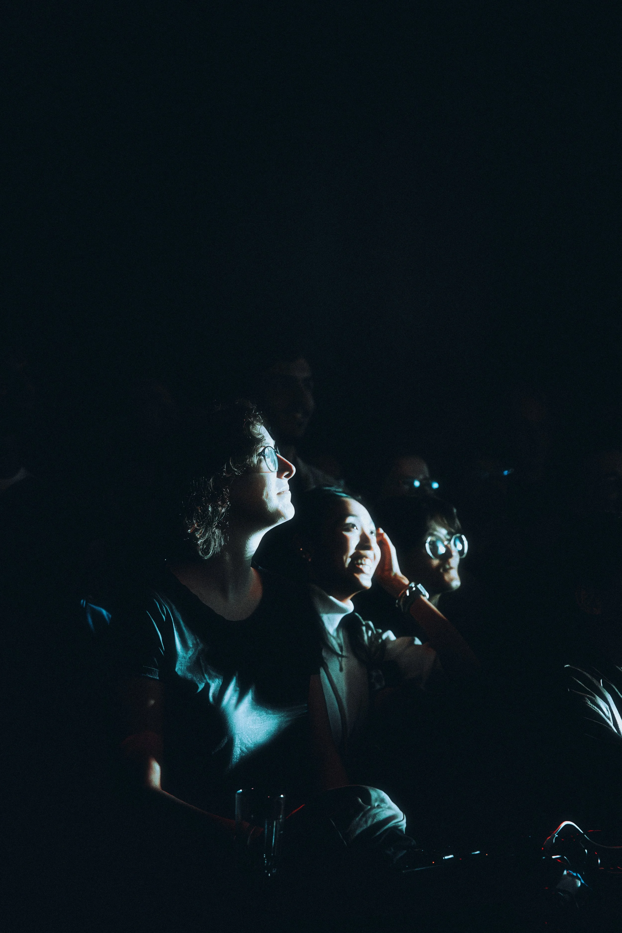 A group of people in a dark room watching a screen with expressions of surprise and awe.