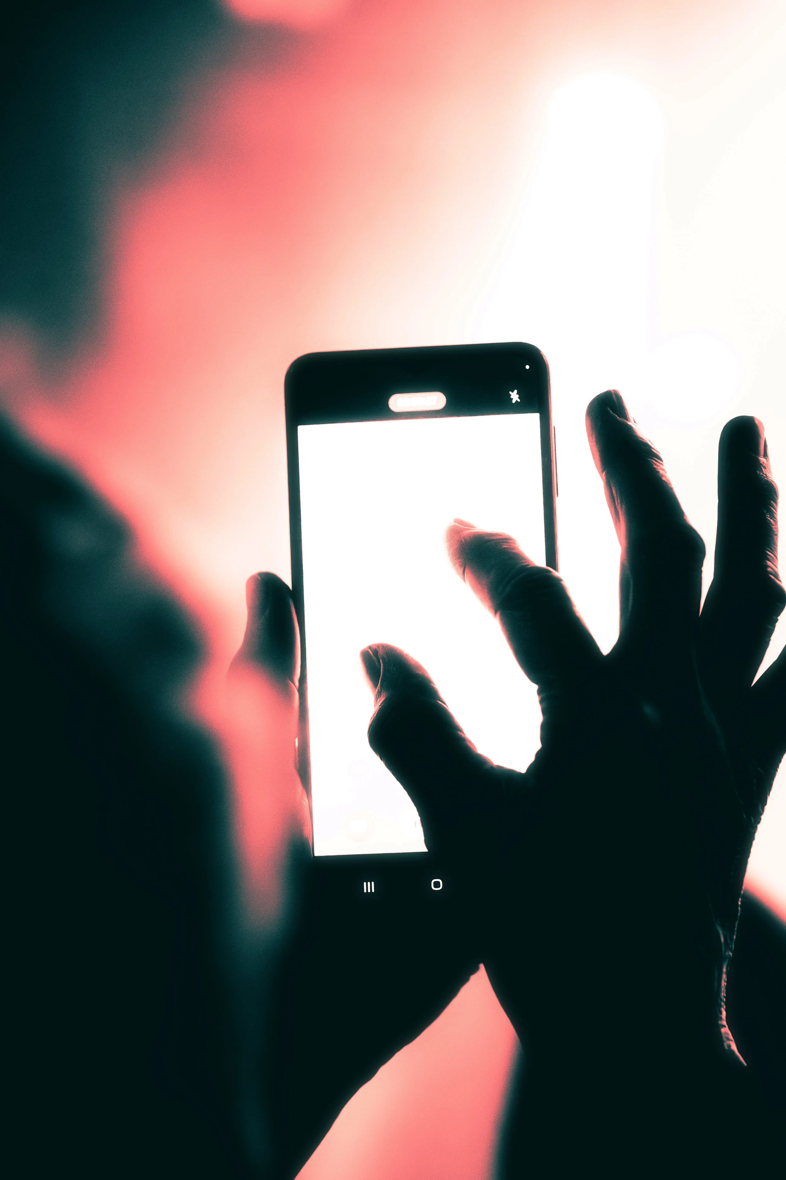 Person taking a photo of a bright light with a smartphone, backlit and silhouetted hand visible.