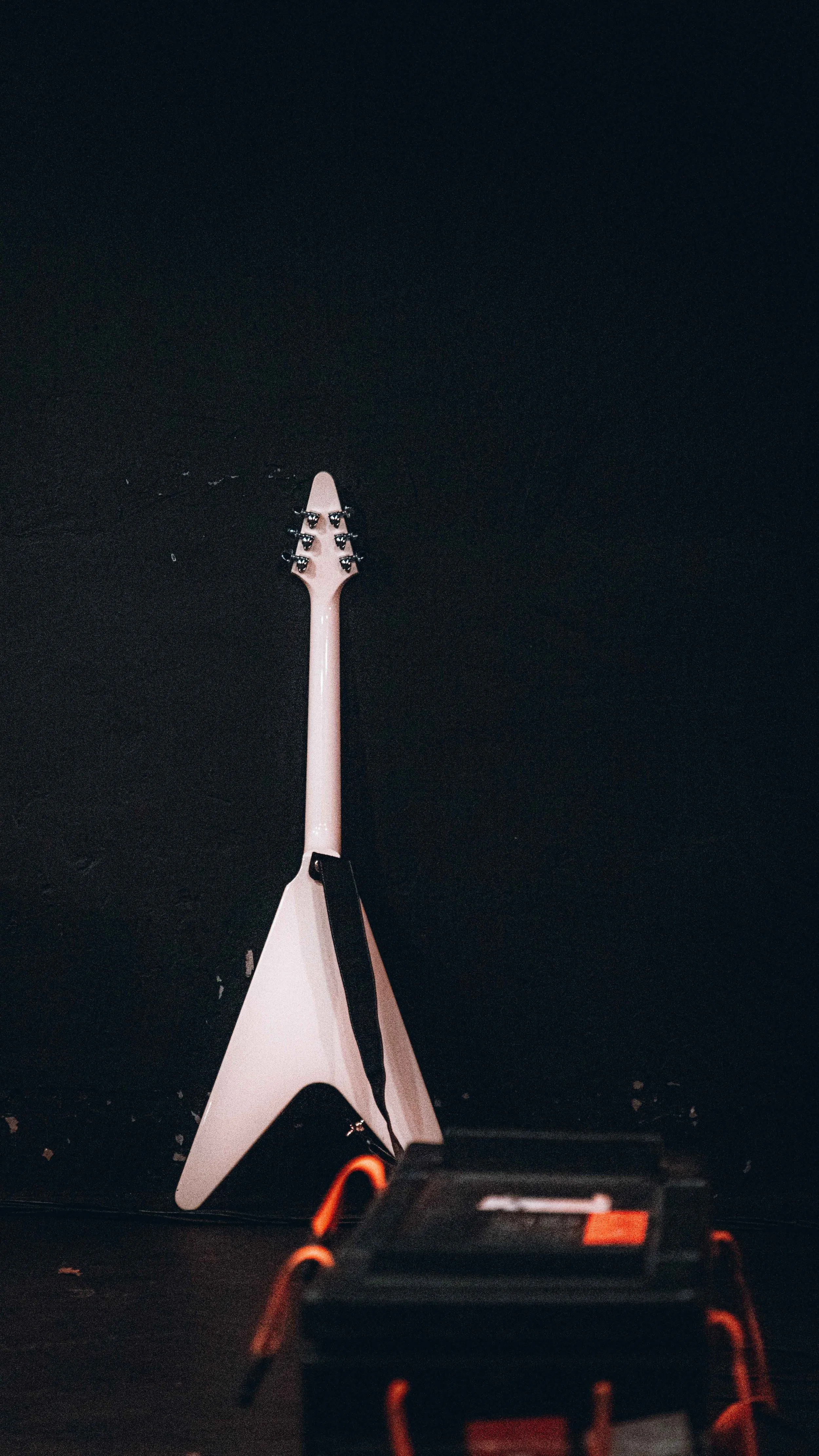 Electric guitar leaning against a dark wall with a black amplifier in the foreground.