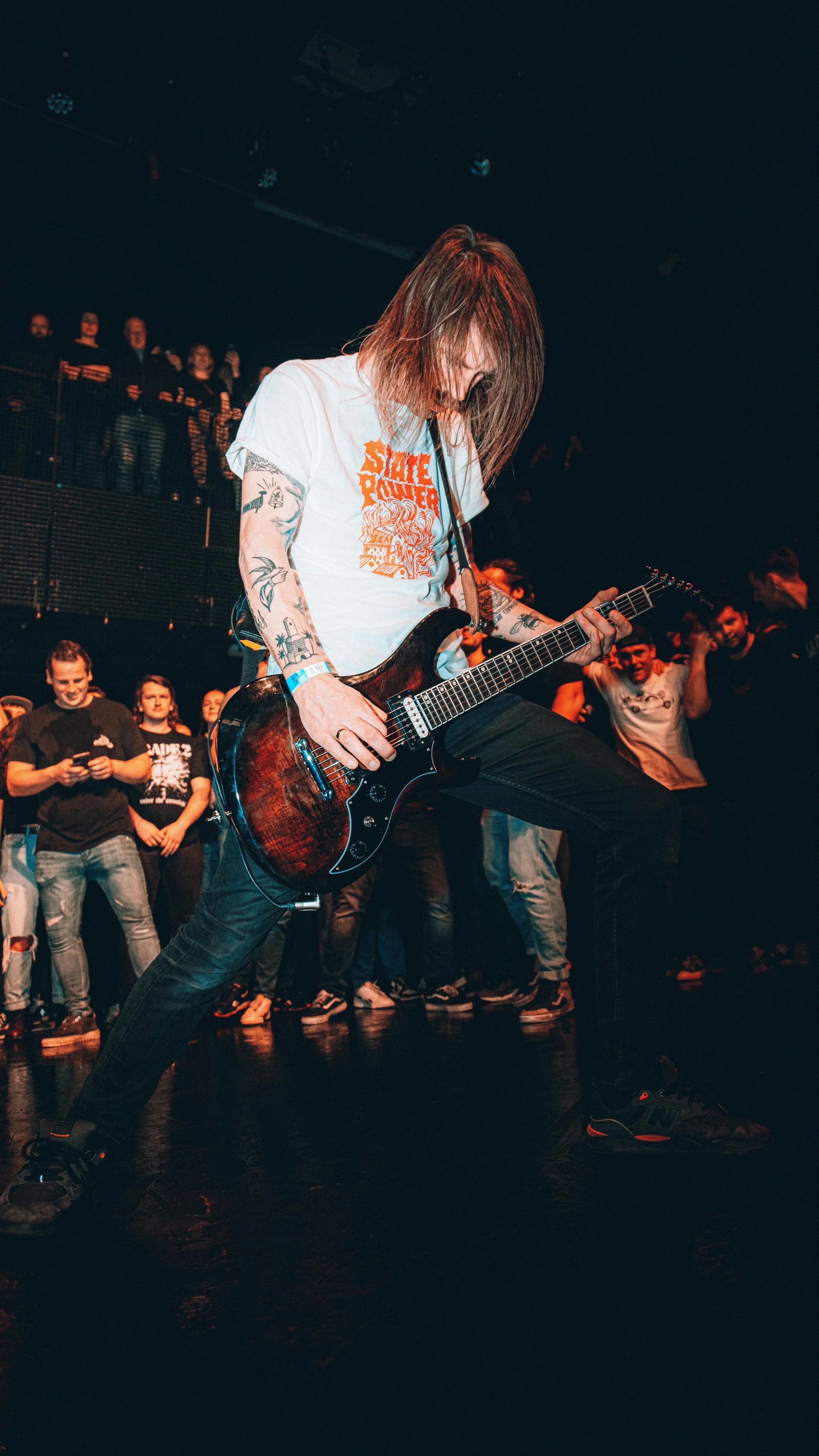 A guitarist performing on stage at a concert, surrounded by an audience watching and taking pictures.