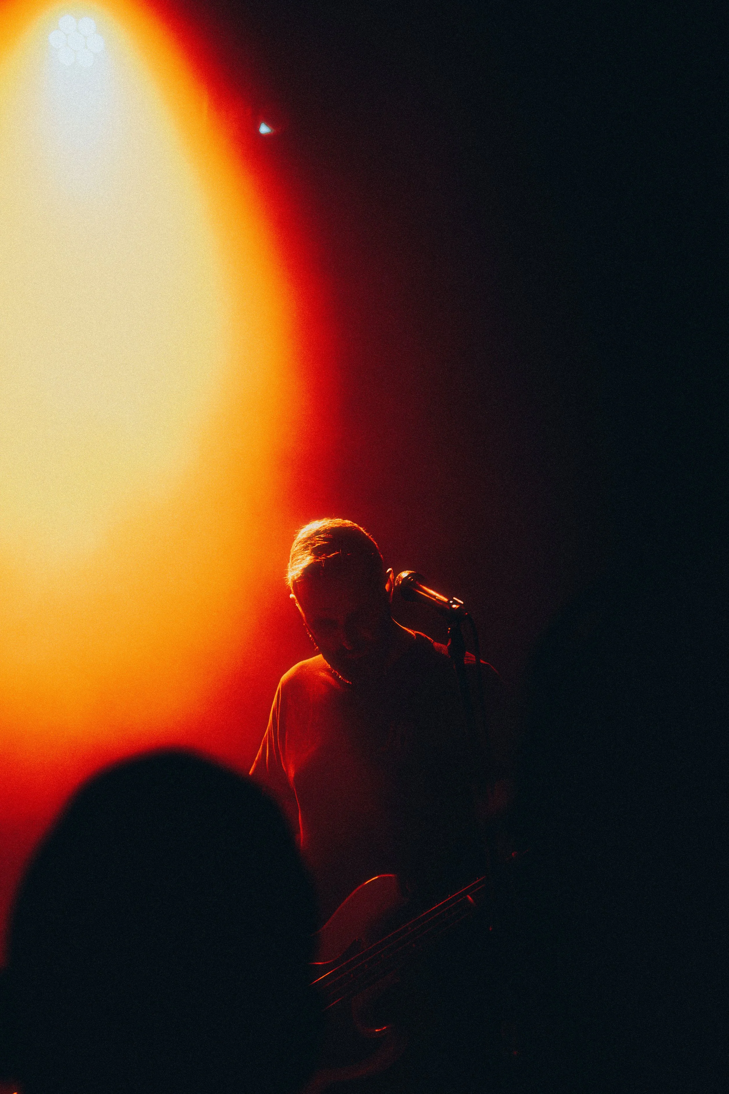 Silhouette of a musician playing guitar on stage under warm, red and yellow lighting with a dark background.