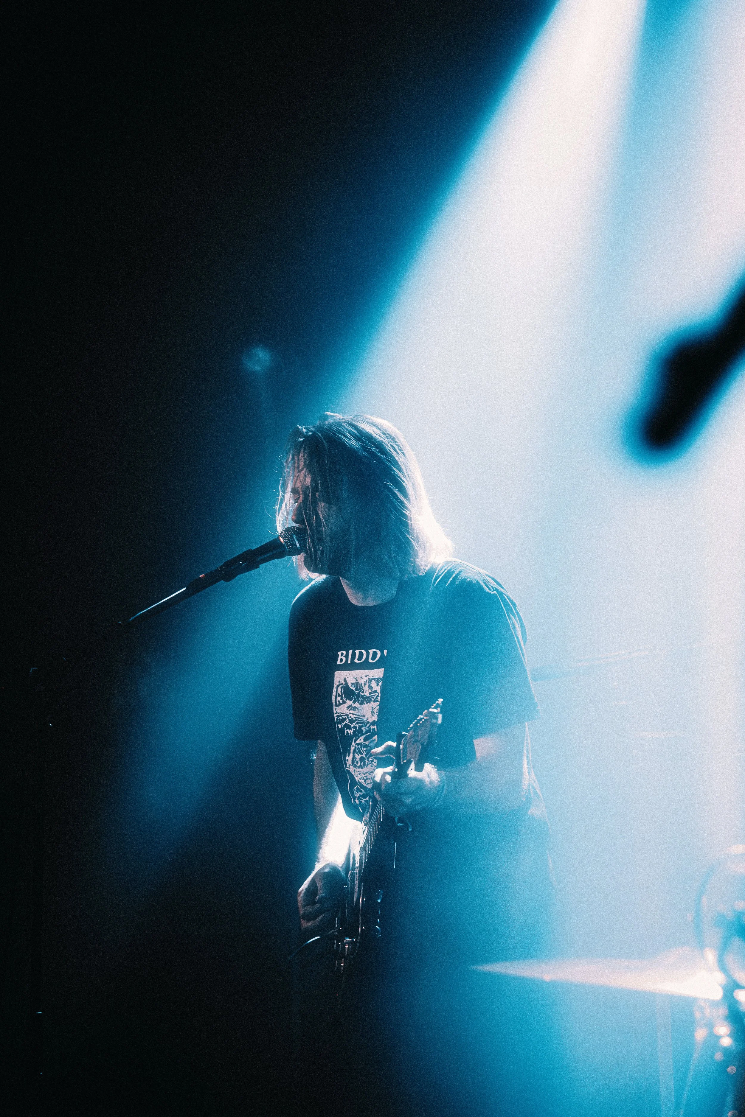 Person performing on stage with a guitar, under a spotlight with a dark background.