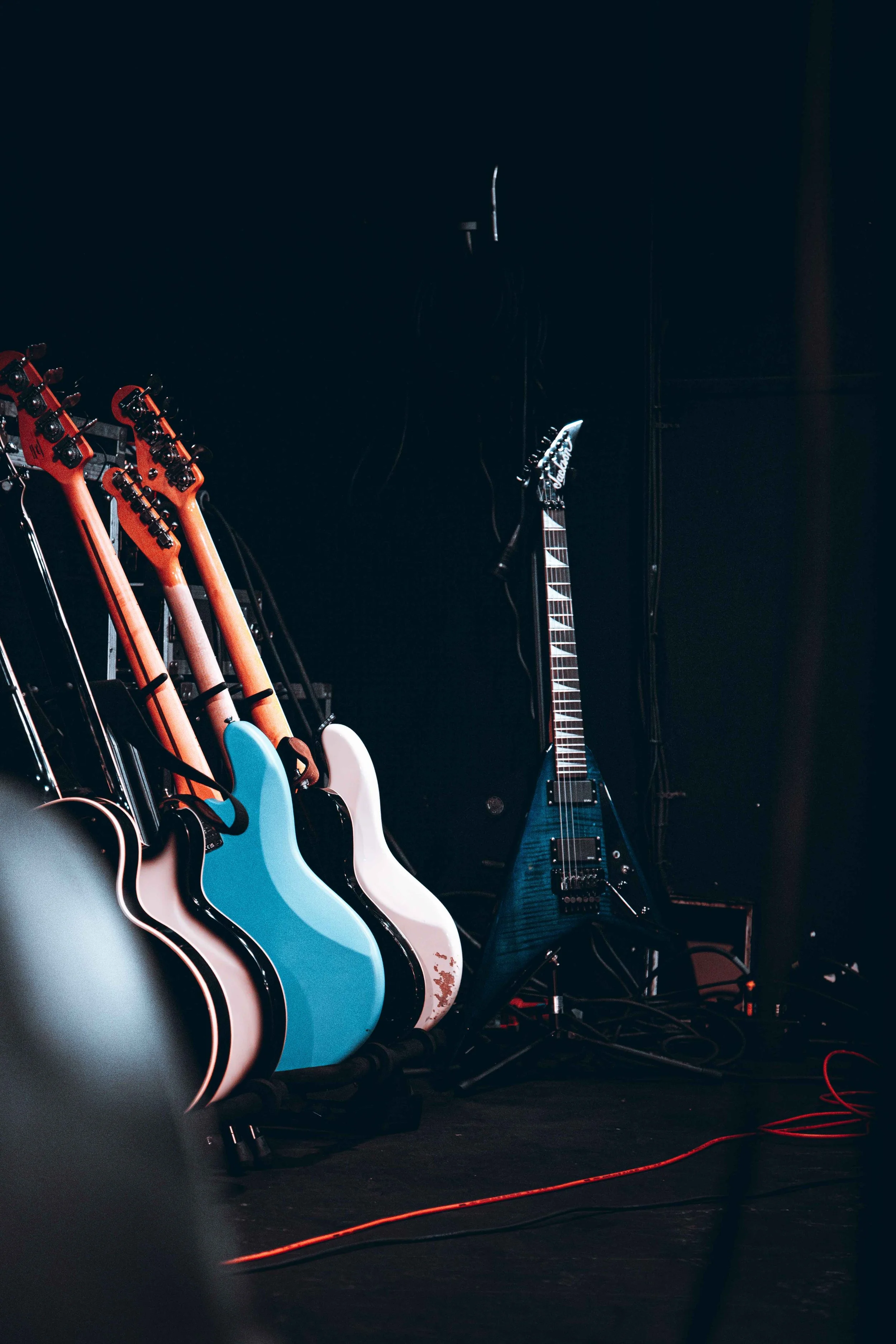 A row of acoustic guitars and an electric guitar set against a black background, with guitar cables on the floor.