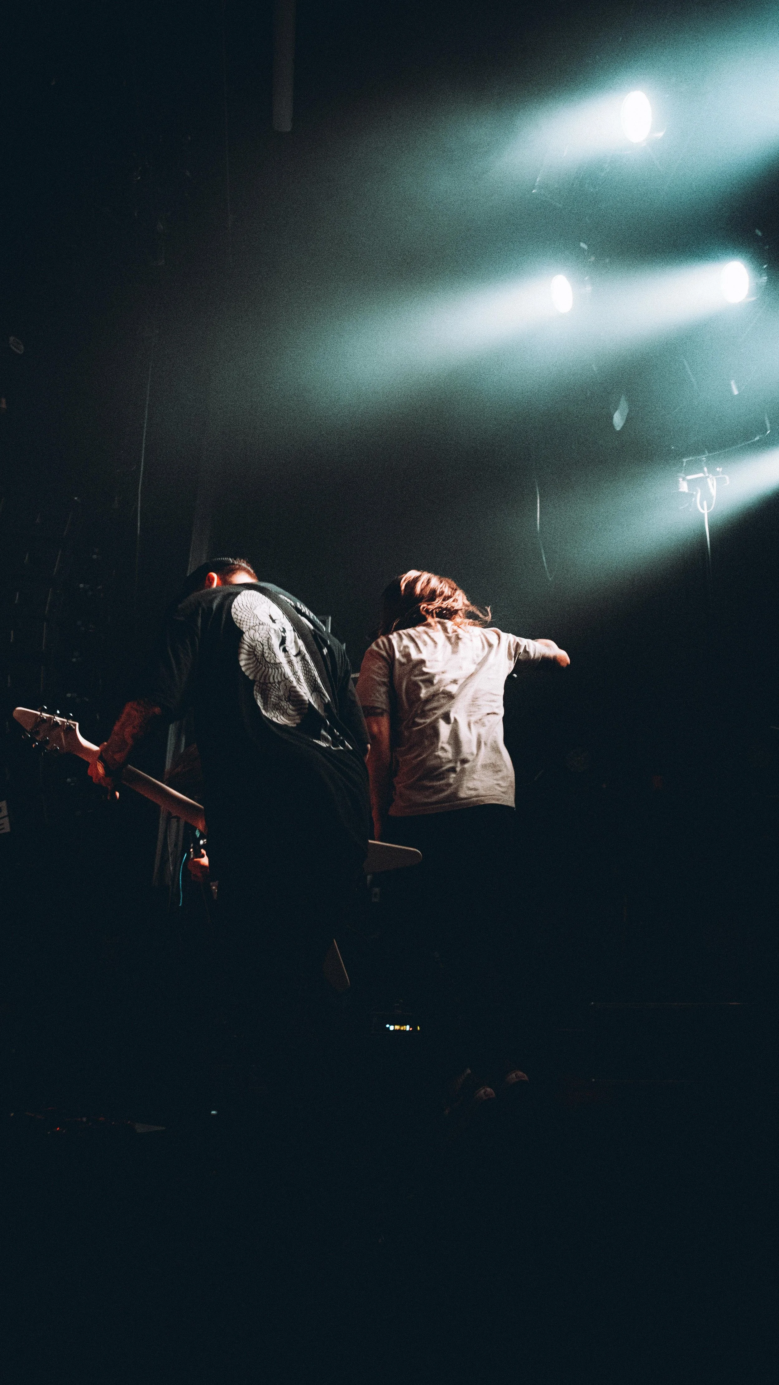 Two musicians performing on stage with bright lights shining down on them.