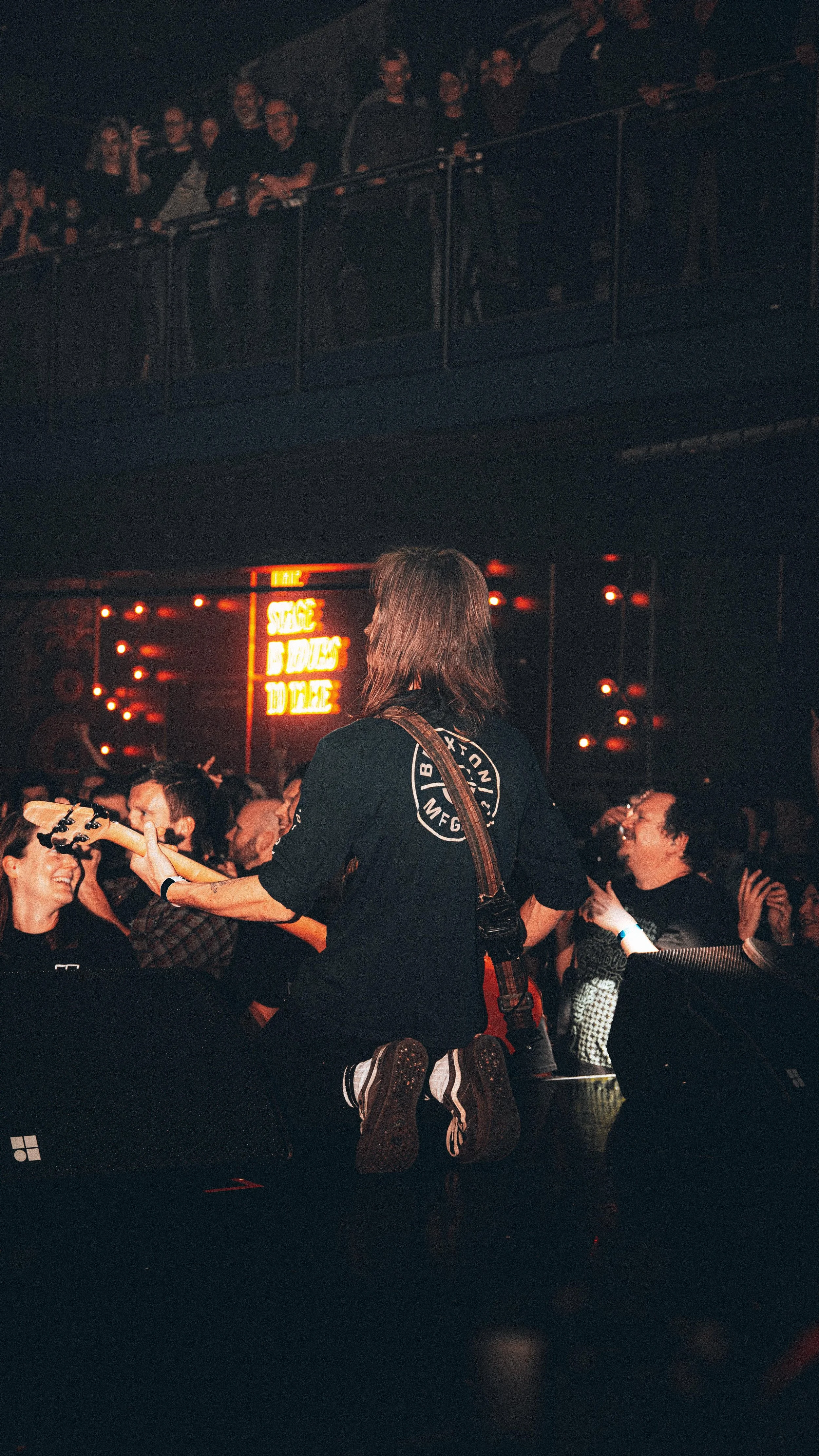 A musician kneeling on stage playing an electric guitar at a concert, surrounded by an audience that is enjoying the performance.