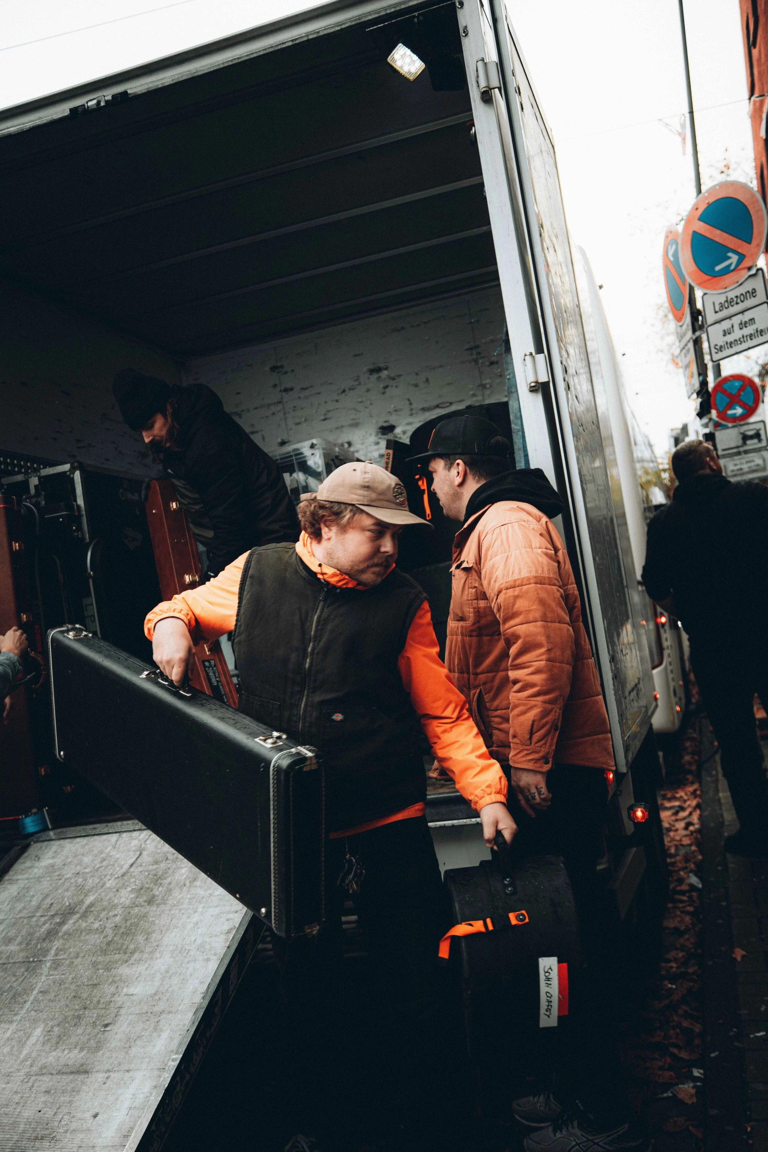 People loading equipment from a truck on a city street with signs indicating loading zone.