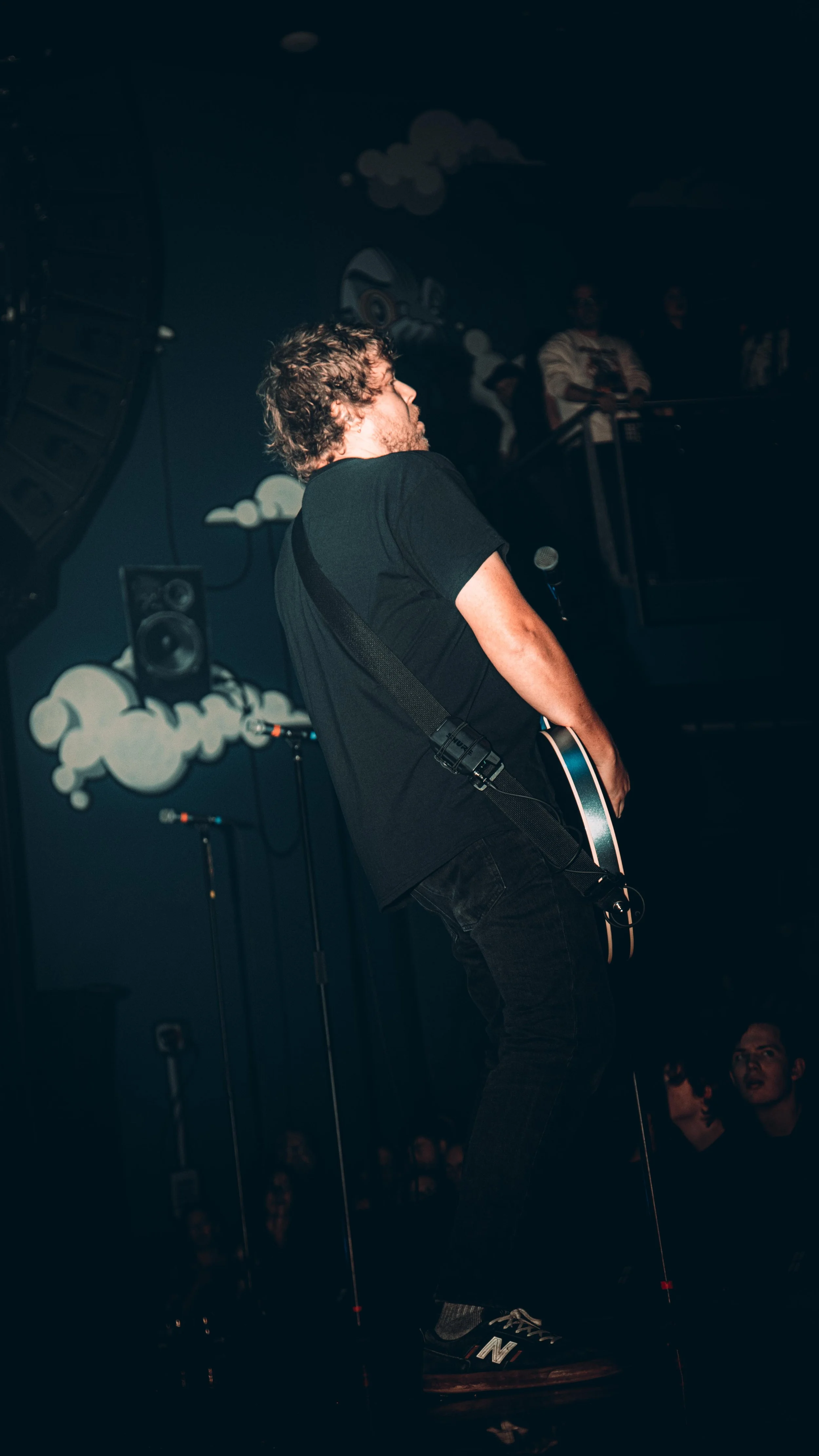 Musician playing guitar during a live performance, with dark background and stage lights