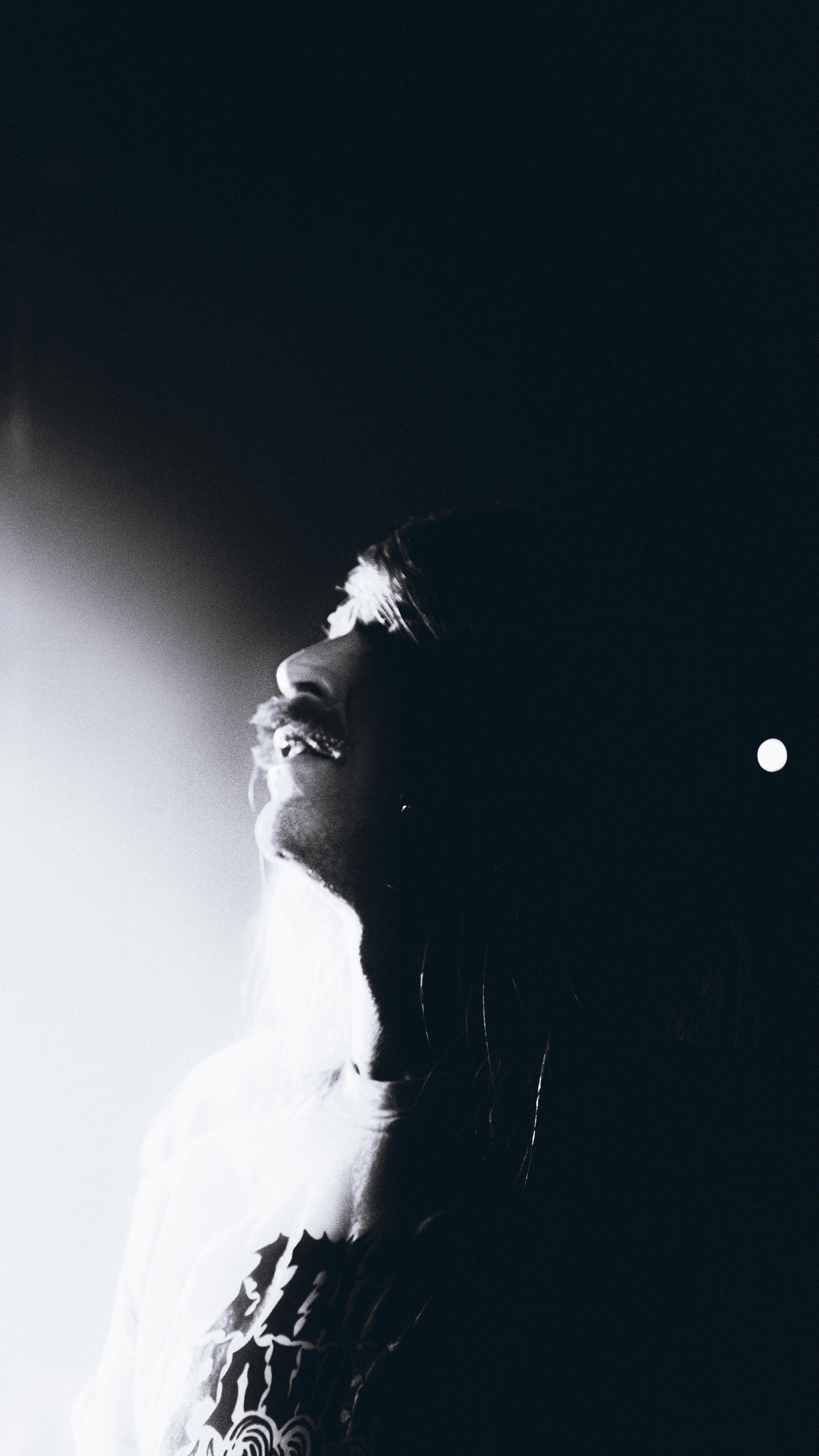 Black and white photo of a person with dreadlocks, smiling, with the left side lit and the right side in shadow, against a dark background.
