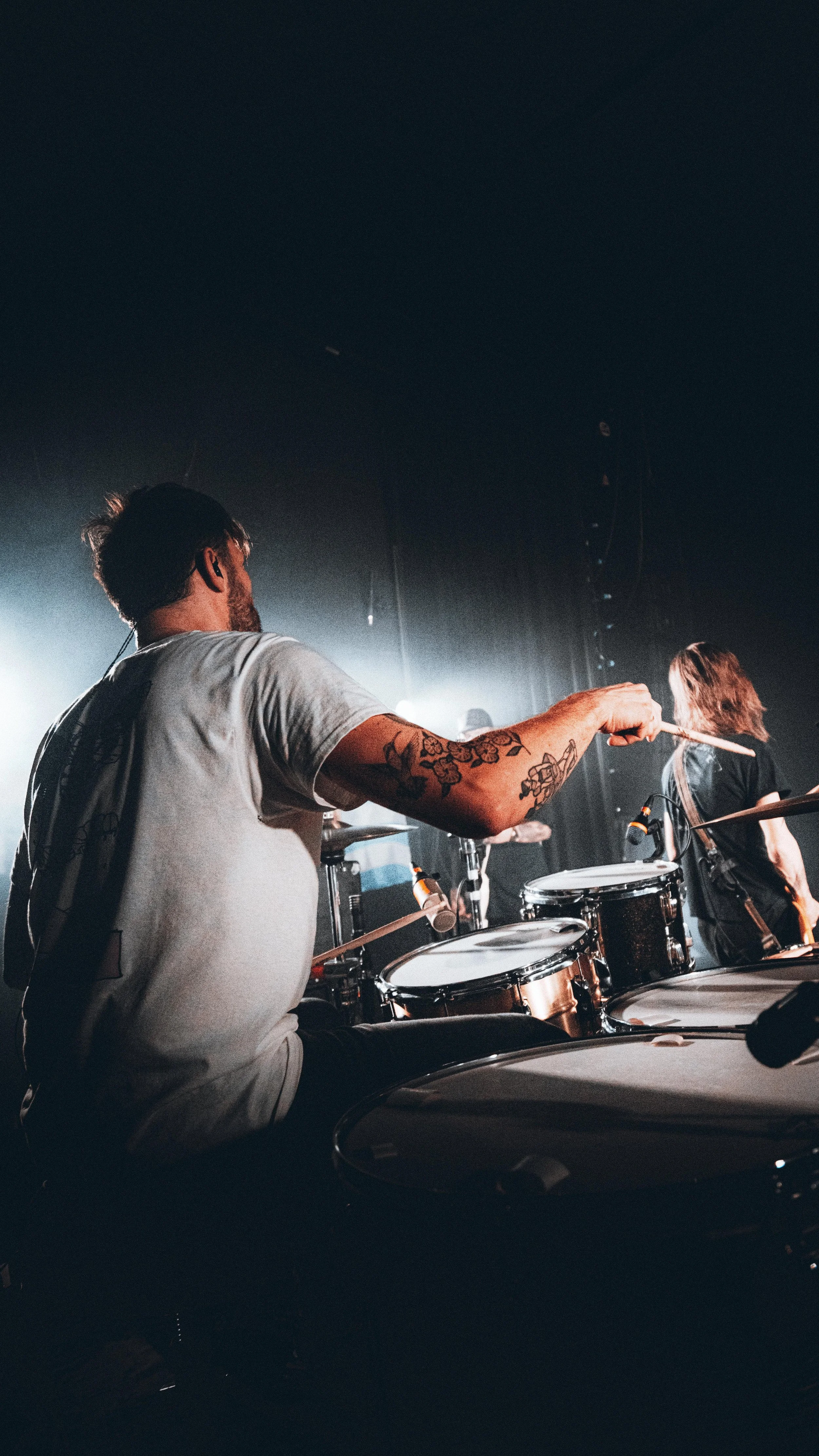 Musician playing drums on stage with spotlight and mudrooms.