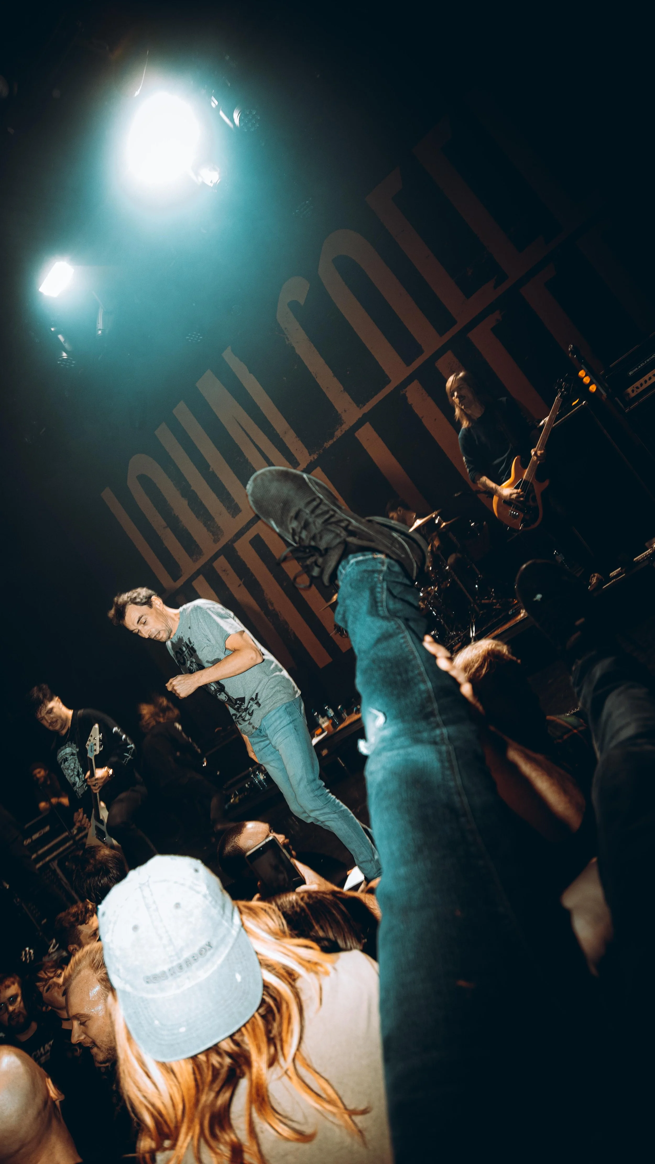 Band performing on stage at a concert with audience members raising hands and taking photos.