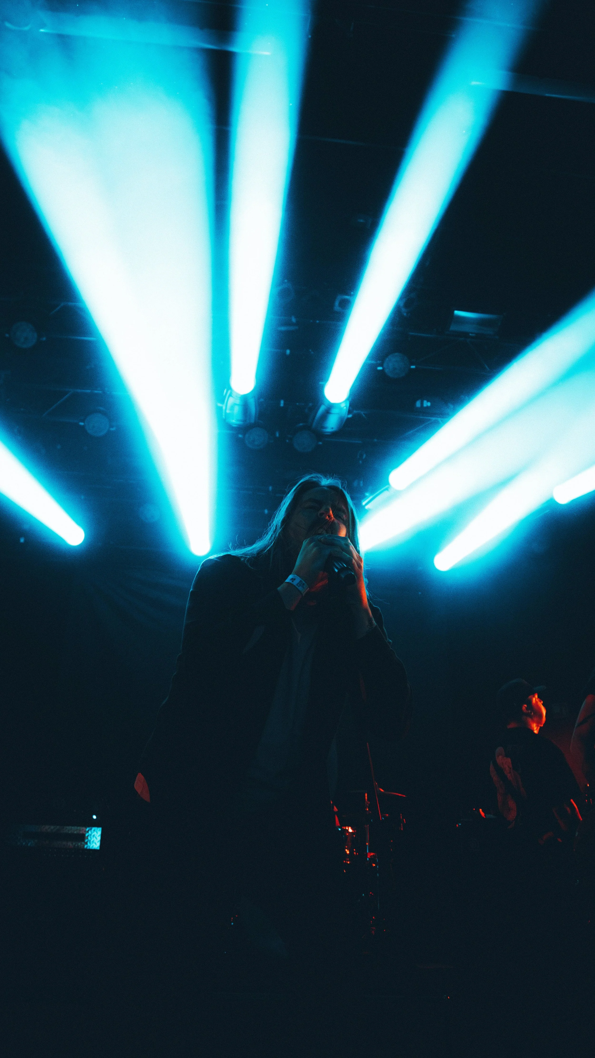 A person holding a microphone on stage with blue and white lights shining behind them during a concert or performance.