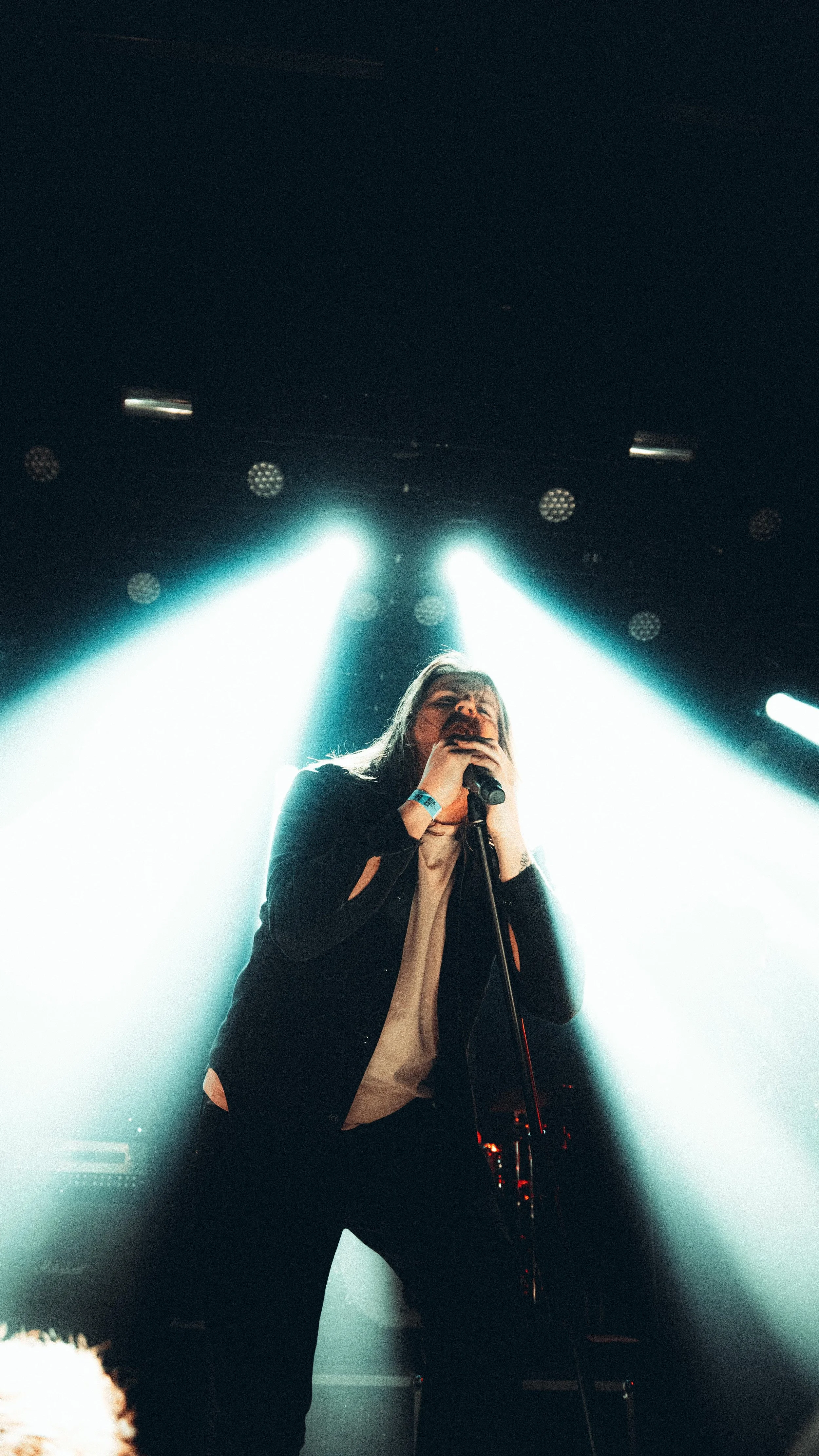 A female singer performing on stage with bright lights shining behind her.