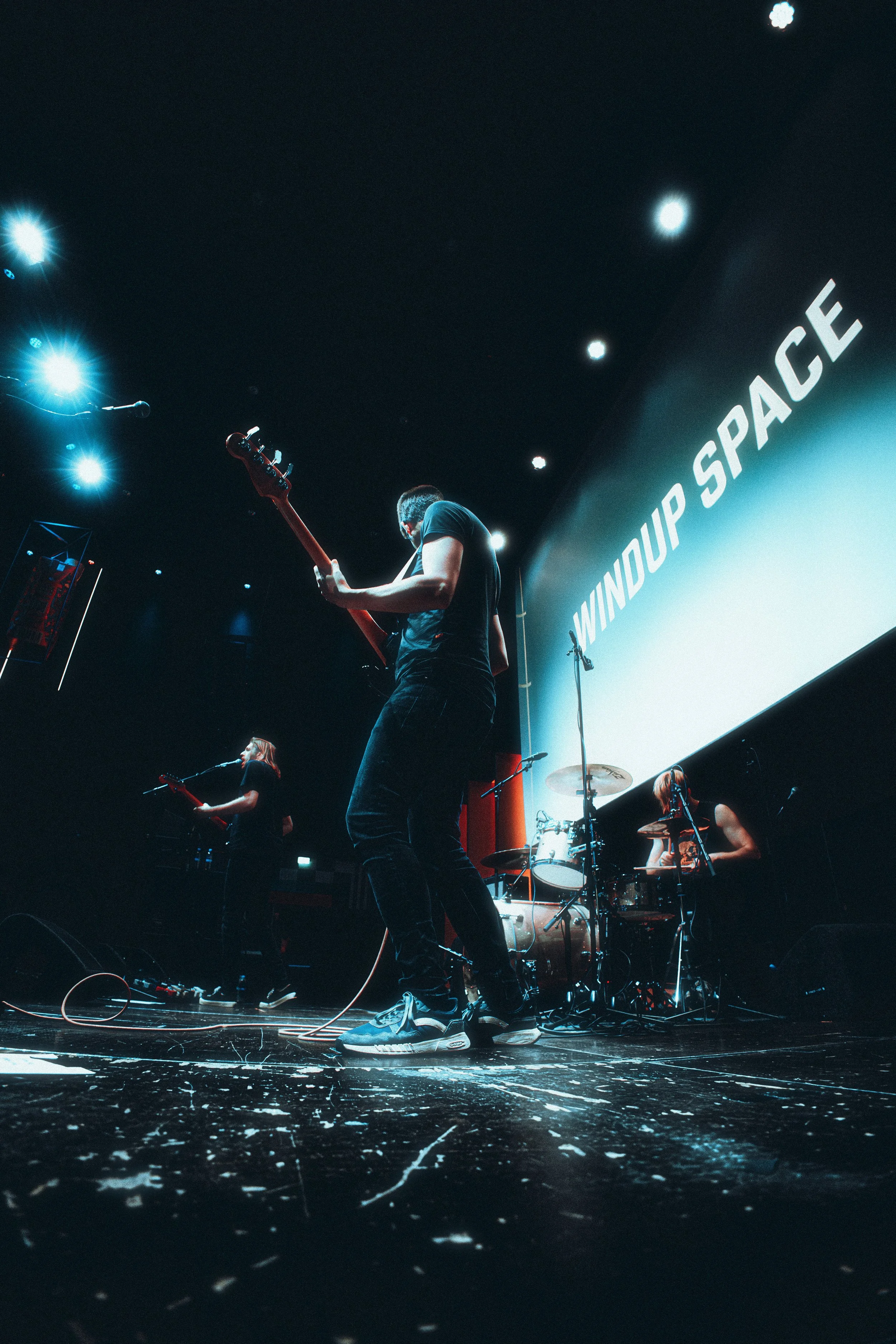 Musicians performing on stage with a large screen displaying 'WINDUP SPACE' in the background.
