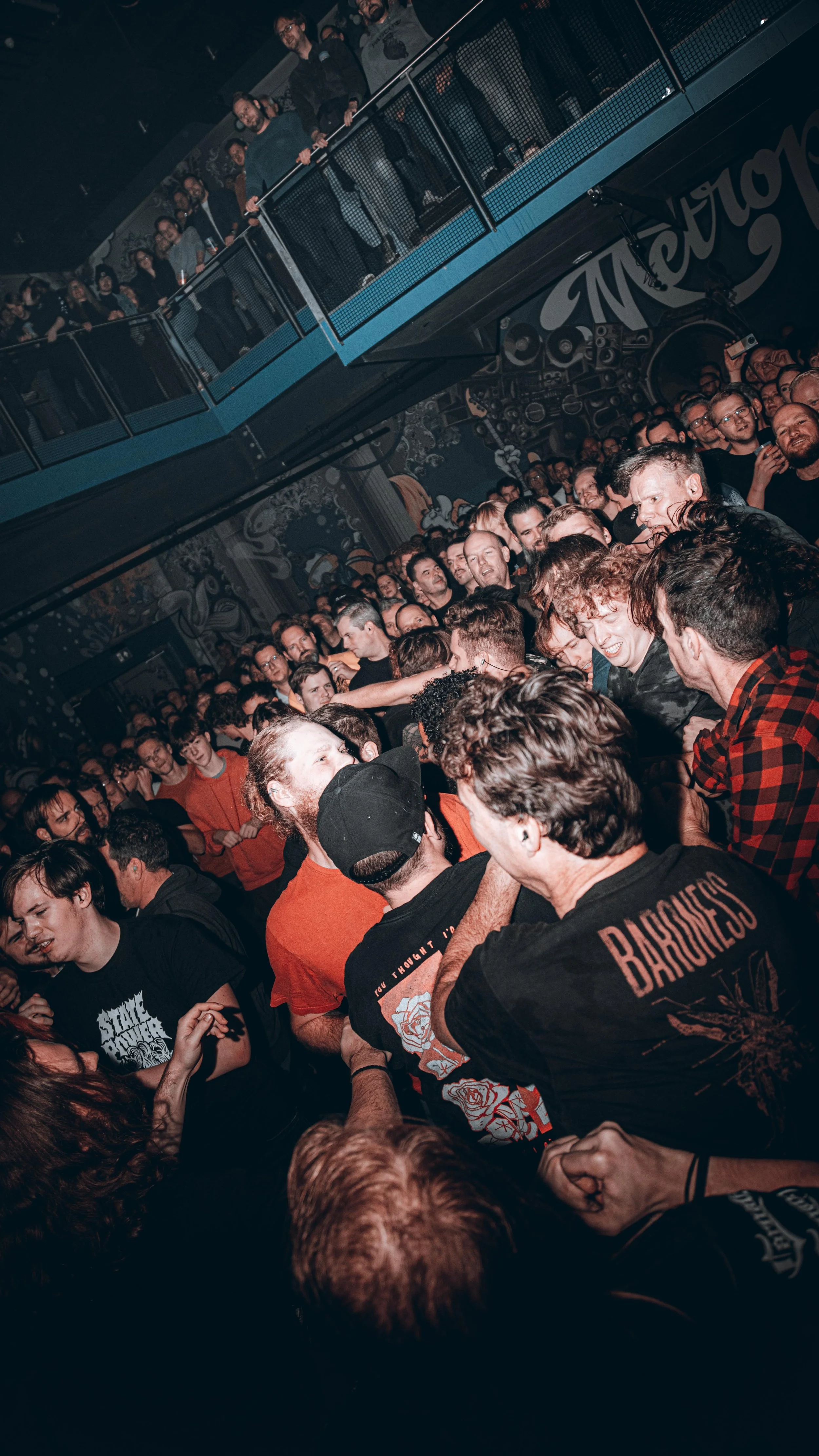 Crowd of people at a concert or music event, with some dancing and enjoying the music, in a dimly lit venue with graffiti-style art on the walls.