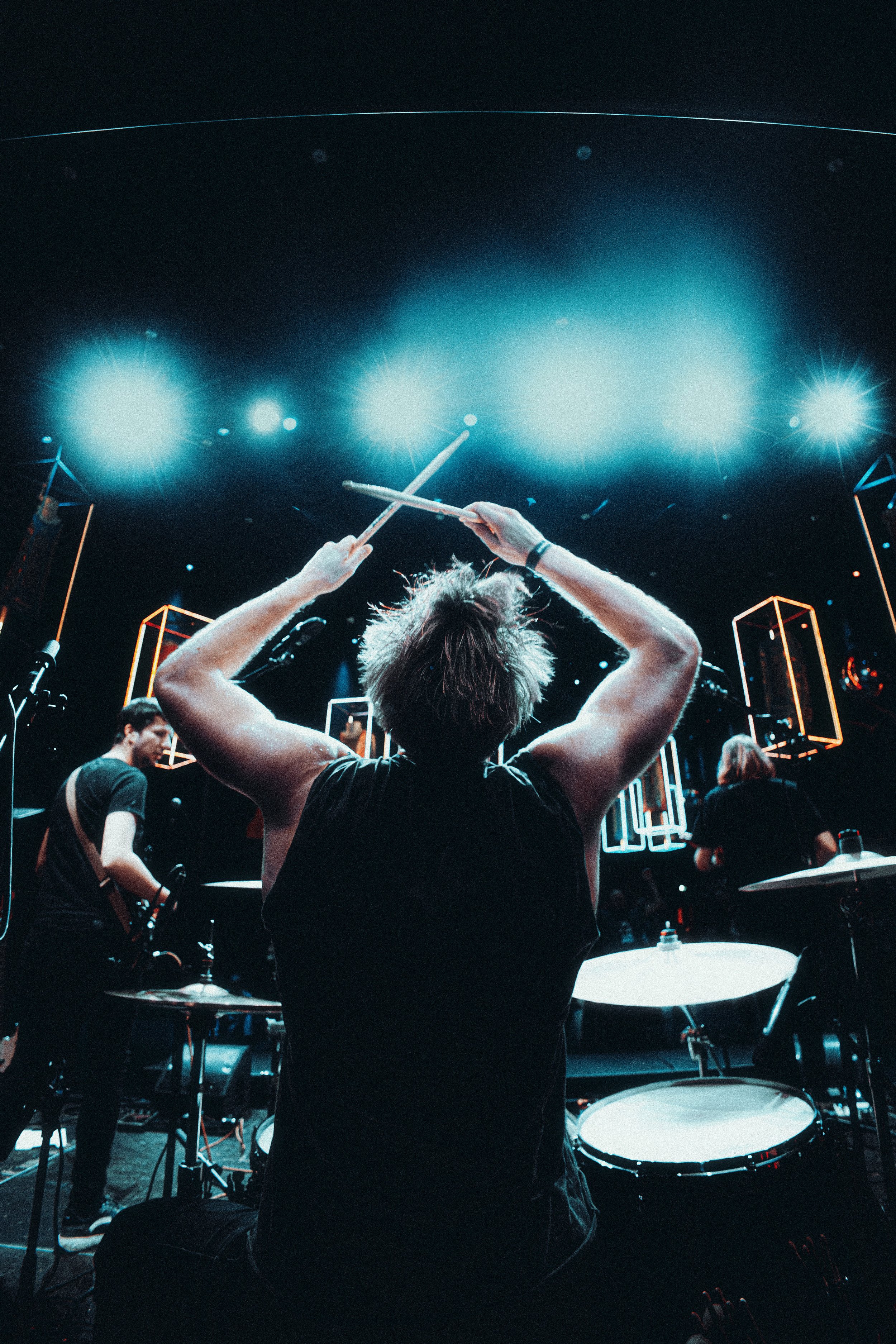 Musician playing drums on stage with bright blue lights and geometric stage design.