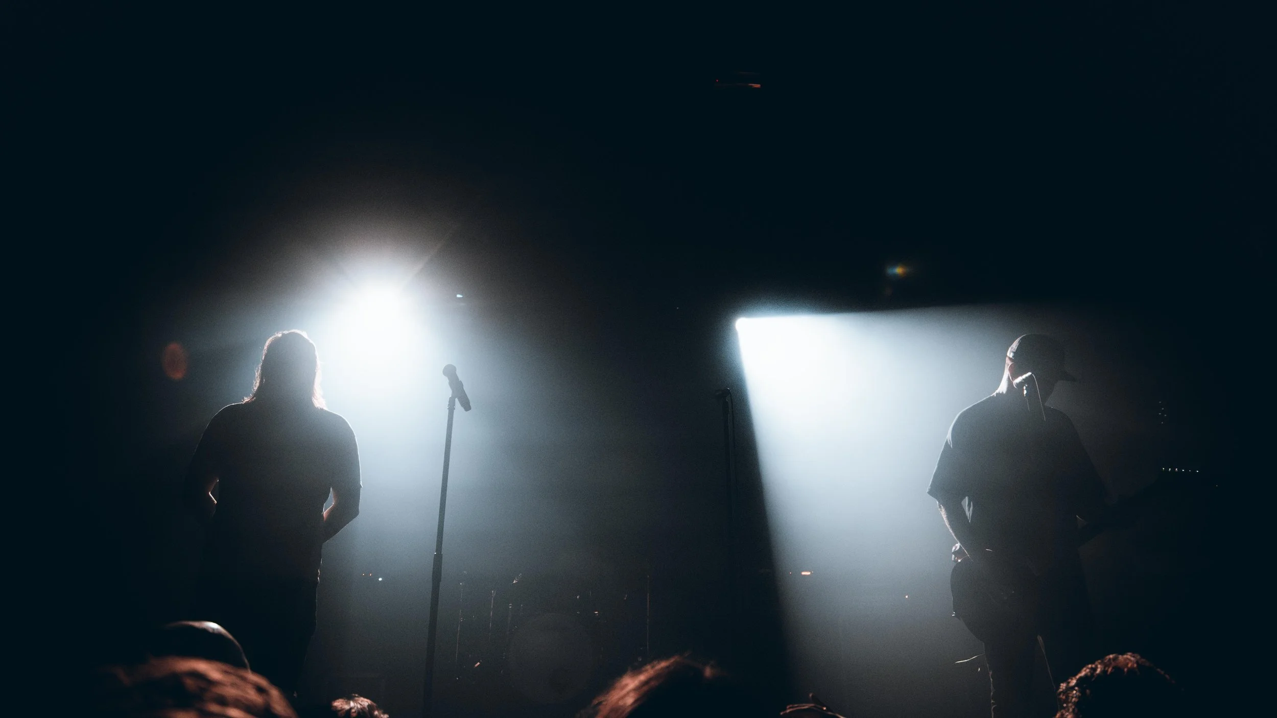 Silhouettes of two musicians on stage with bright lights shining behind them during a concert.