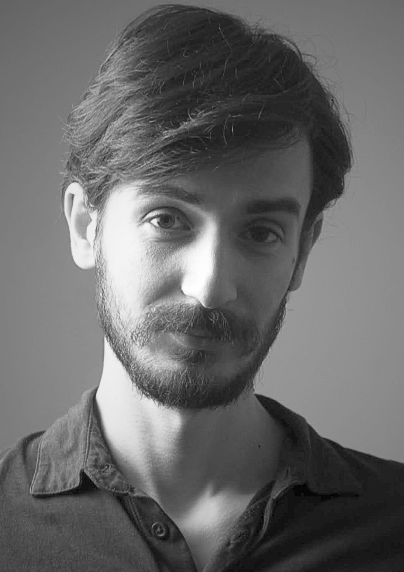 Black and white portrait of a man with wavy hair and a beard, wearing a collared shirt.