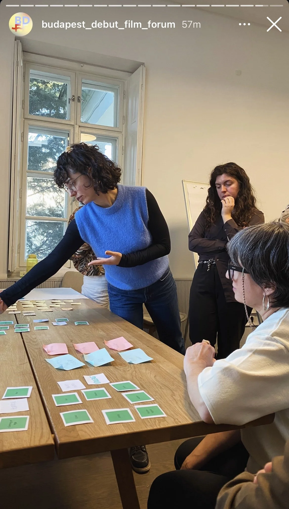 A group of women participating in a collaborative activity around a wooden table with colored flashcards and sticky notes in a well-lit room with large windows.