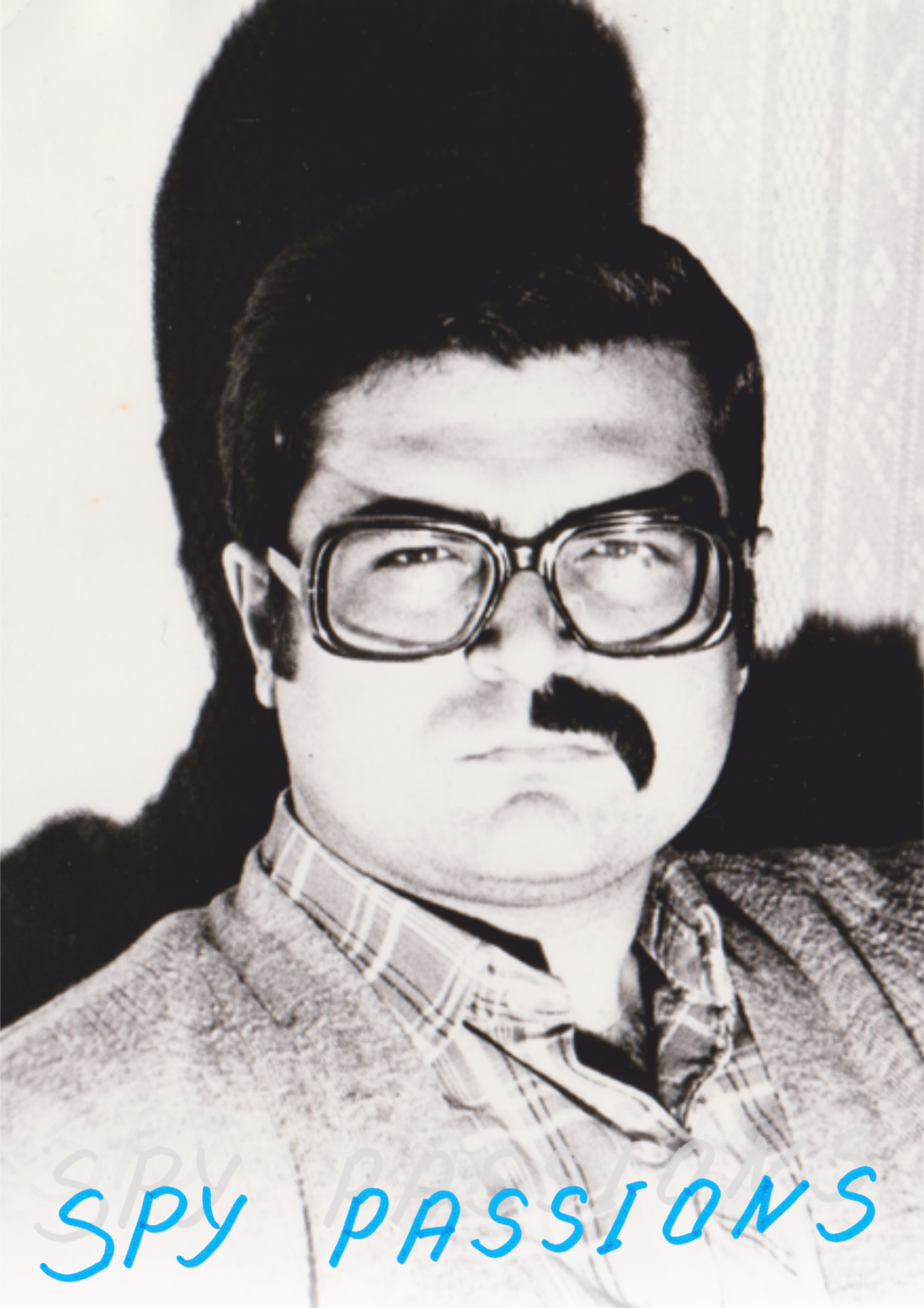Black and white photo of a man with glasses, dark hair, and a mustache, wearing a checkered shirt and a sweater, with the words 'spy passions' in blue text at the bottom.