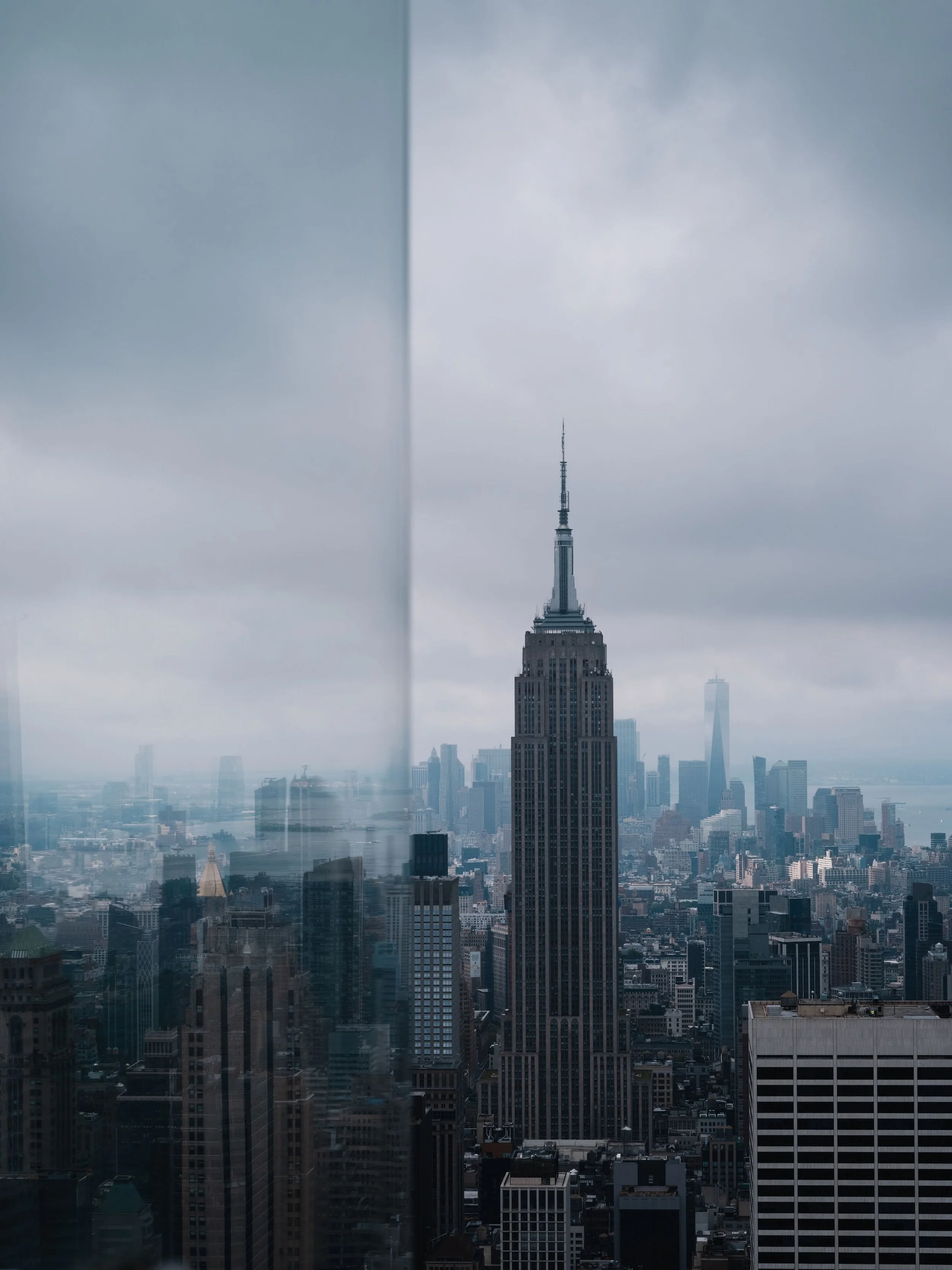 Photo de la skyline de New York, vue sur l'Empire State Building entouré d'autres gratte-ciel, sous un ciel nuageux.