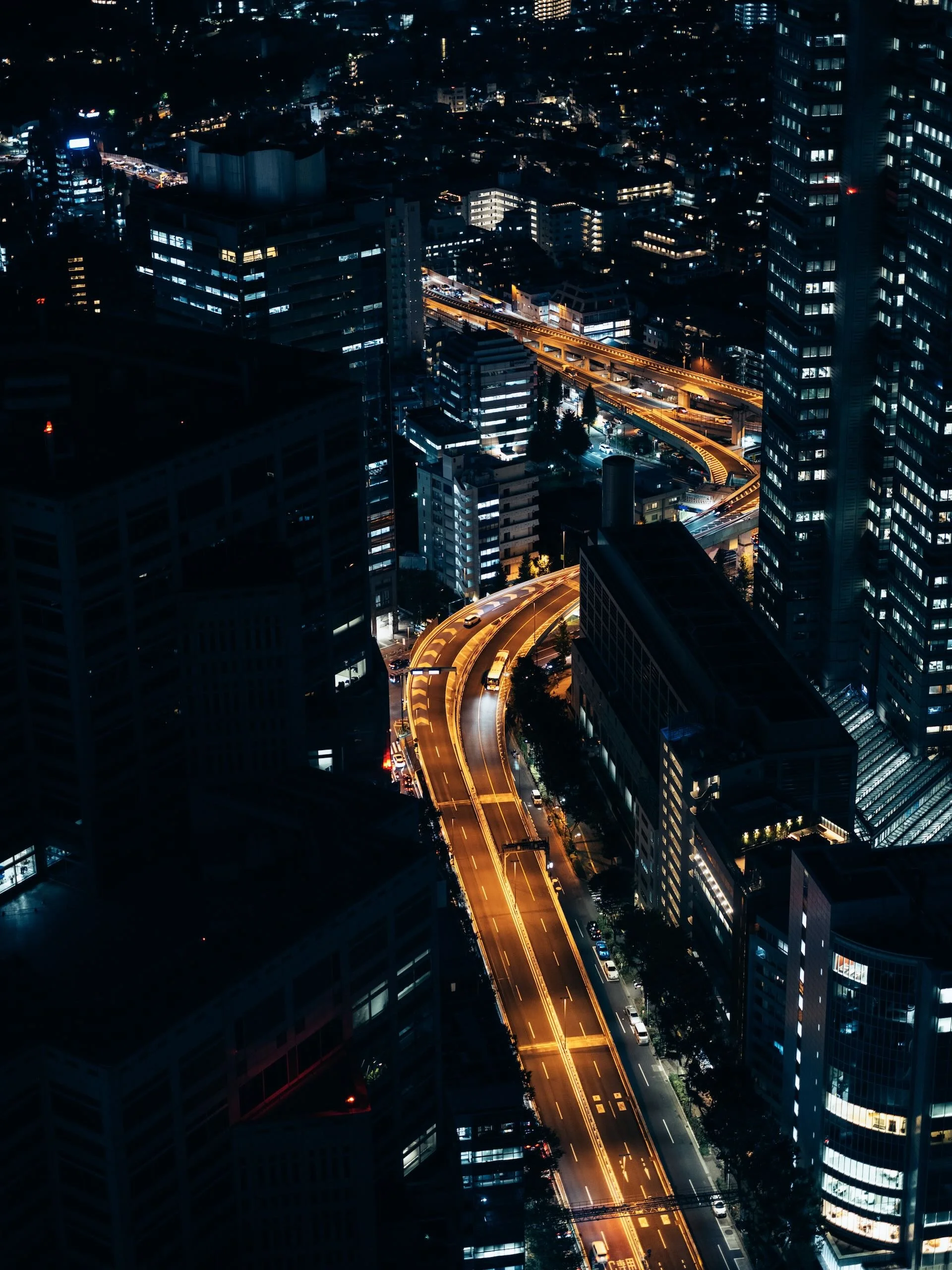 Vue aérienne d'une ville de nuit avec des bâtiments modernes illuminés, des routes éclairées, et beaucoup de gratte-ciel.