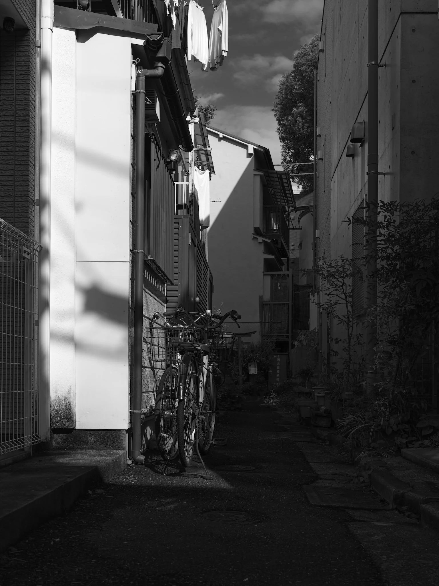 Une ruelle sombre avec un vélo garé contre un mur et des vêtements suspendus à des cordes entre deux bâtiments.